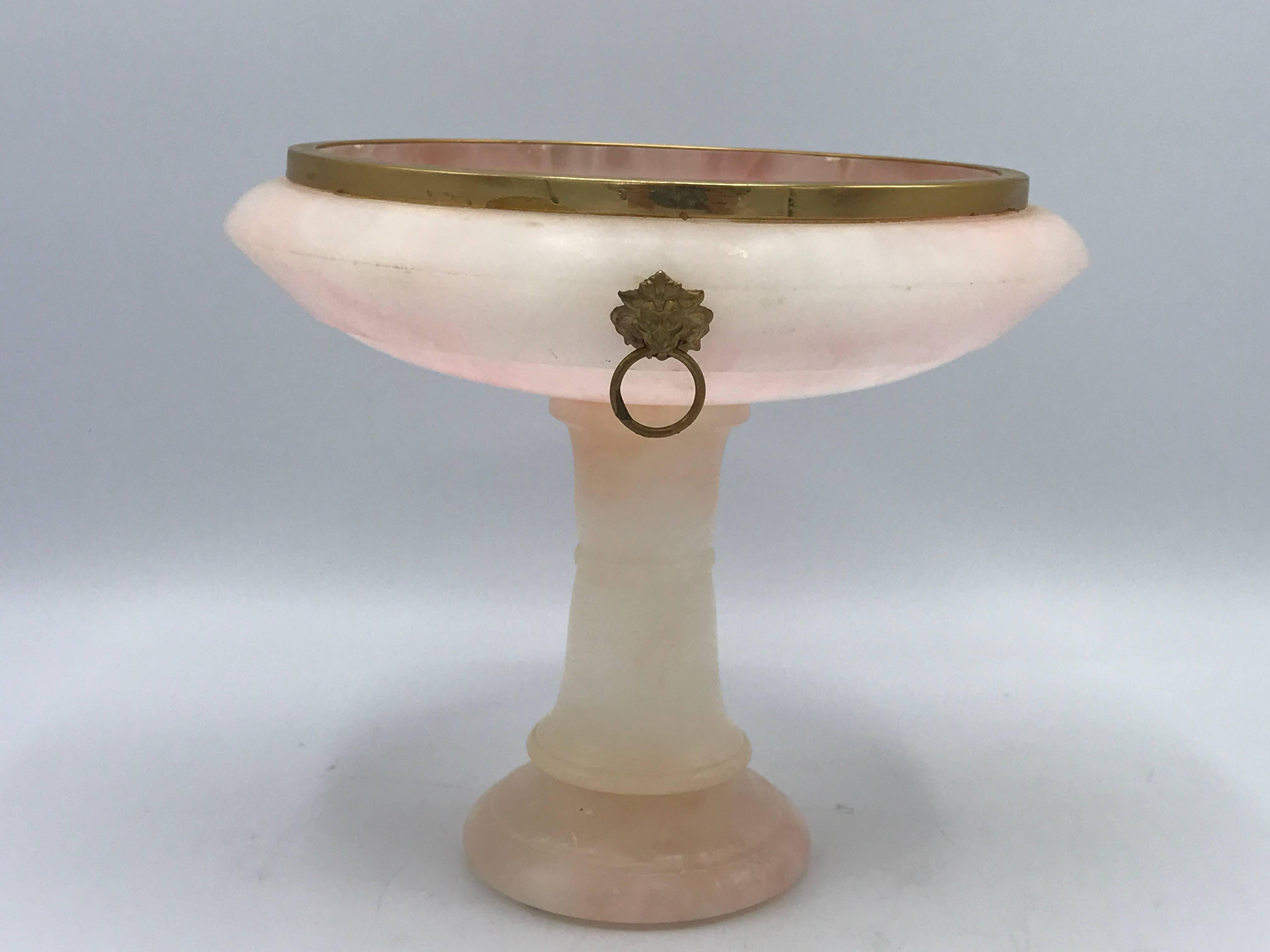 Offered is a fabulous, 1930s Italian pink alabaster urn/bowl on a pedestal. The piece has brass lion head handles and a brass border along the rim. Original sticker on bottom.