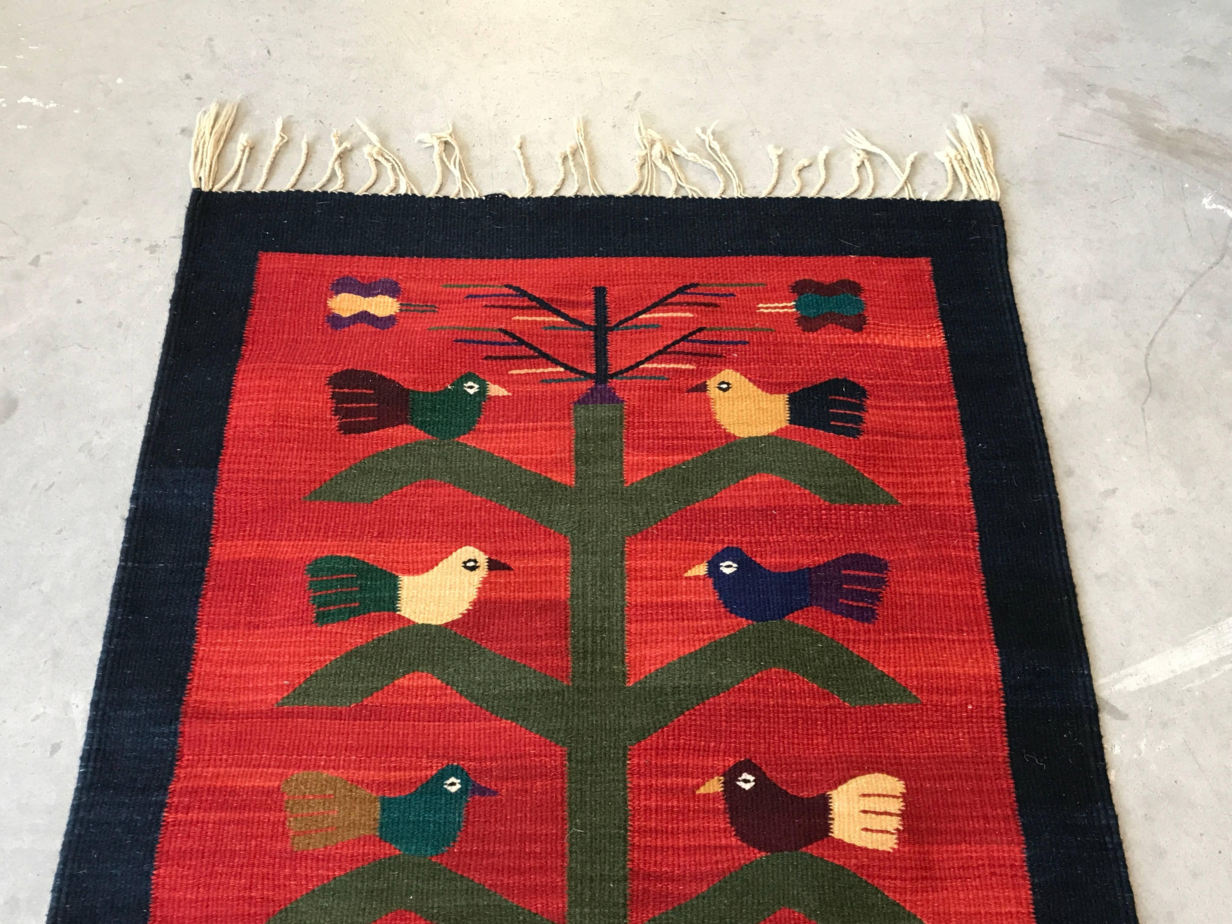 Offered is a fabulous, 1950s red Kilim rug with a polychrome bird and potted plant motif. Some pieces of the fringe needs to be trimmed or re-braided. We suggest a rug pad, or rug tape to prevent slipping.