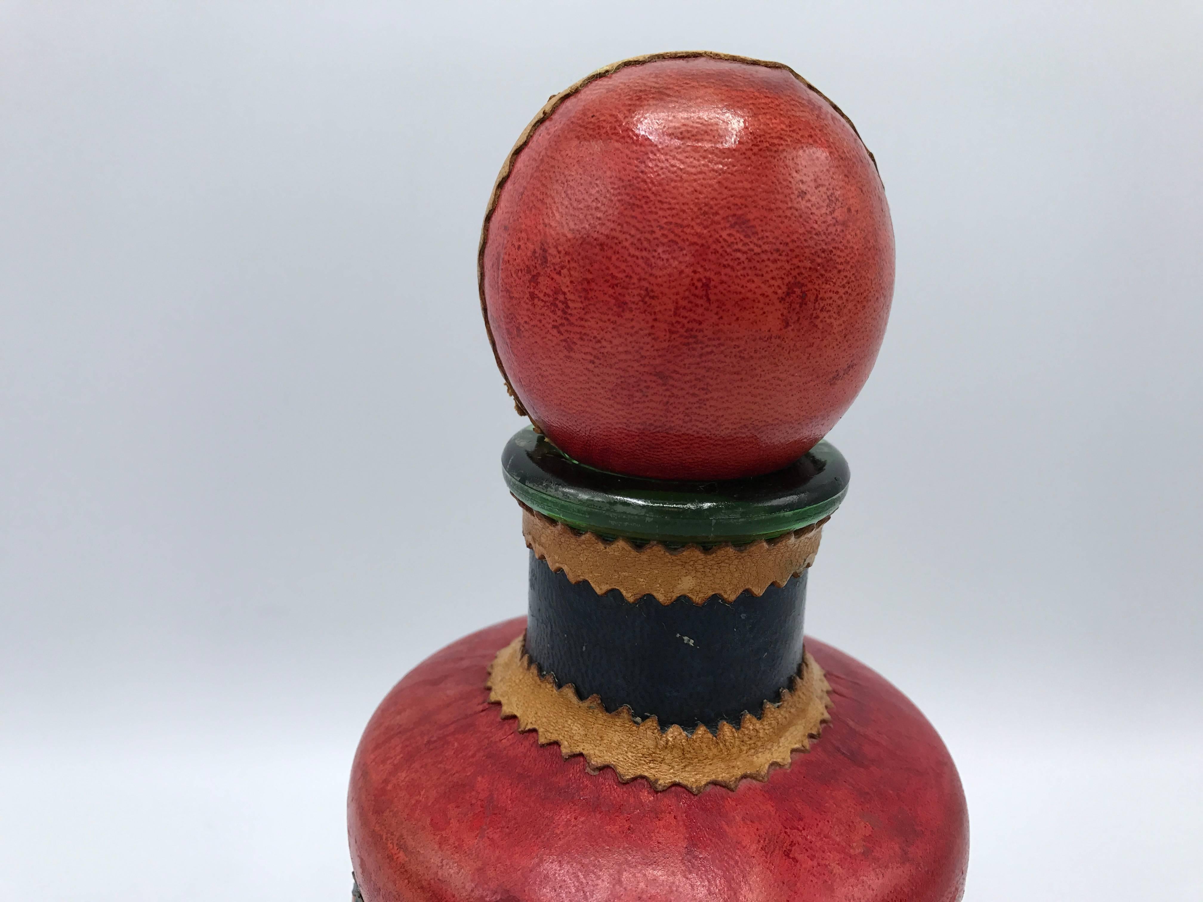 Offered is a gorgeous, 1960s Italian red leather decanter with a brass ship-wheel on the front side. The piece has navy blue and camel leather horizontal stripes from top to bottom. Marked on underside.