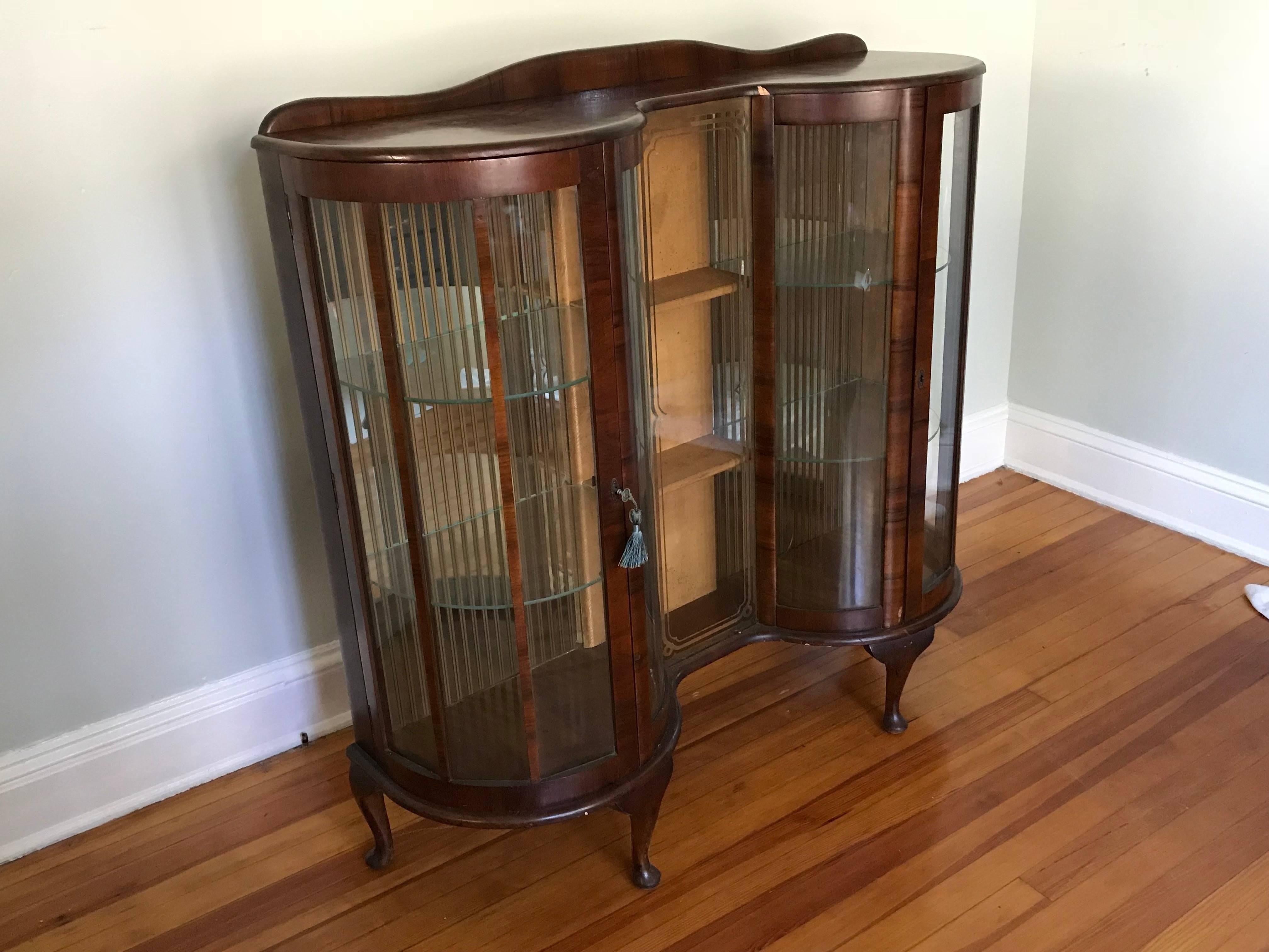 Offered is a beautiful, 1950s English walnut and glass curio display cabinet. The piece had two doors, three levels of shelving, and includes the original key. Marked: 