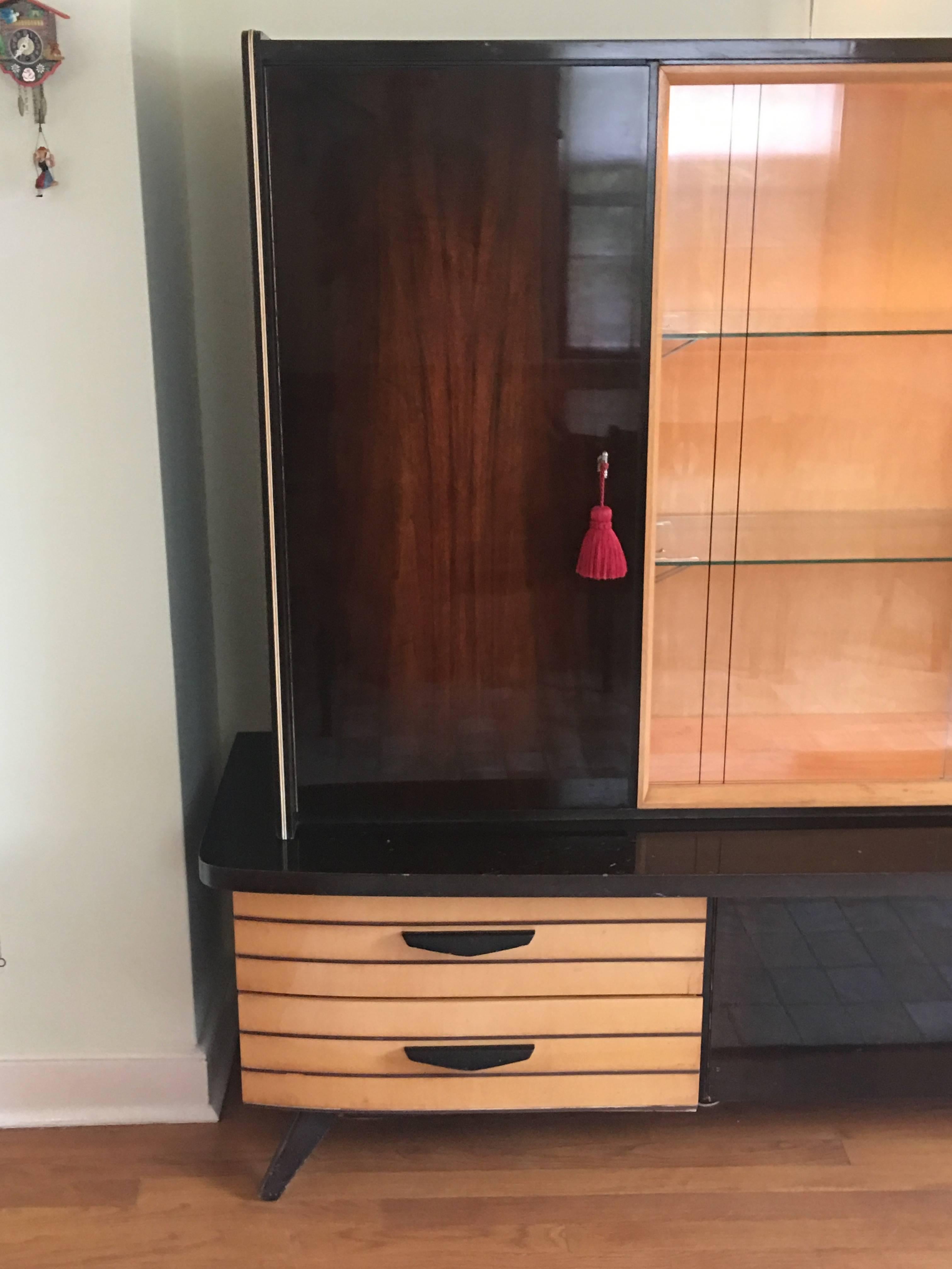 Your storage options are endless in this fabulous, 1950s space-age German shrunk cabinet. Includes center glass sliding doors with glass shelves, lock door cabinets on either side revealing a bar and storage area, drawers on the left bottom, and a