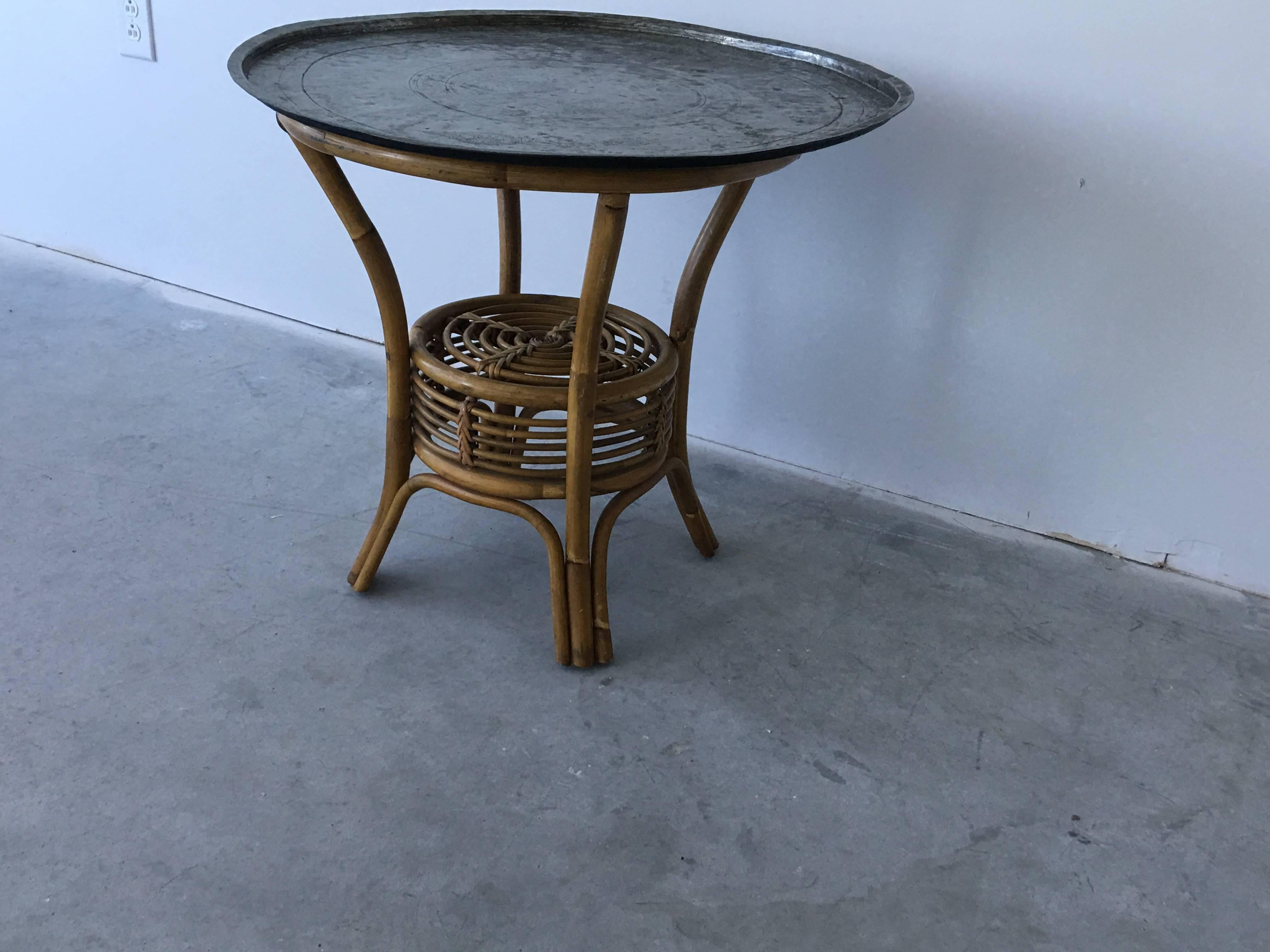 Offered is a beautiful, Mid-Century tray table. The metal tray top is hand-hammered and hand-etched with a mandala and floral motif. We believe the top is antique Moroccan, though the base much more recent (1950s). The base is bamboo and rattan.