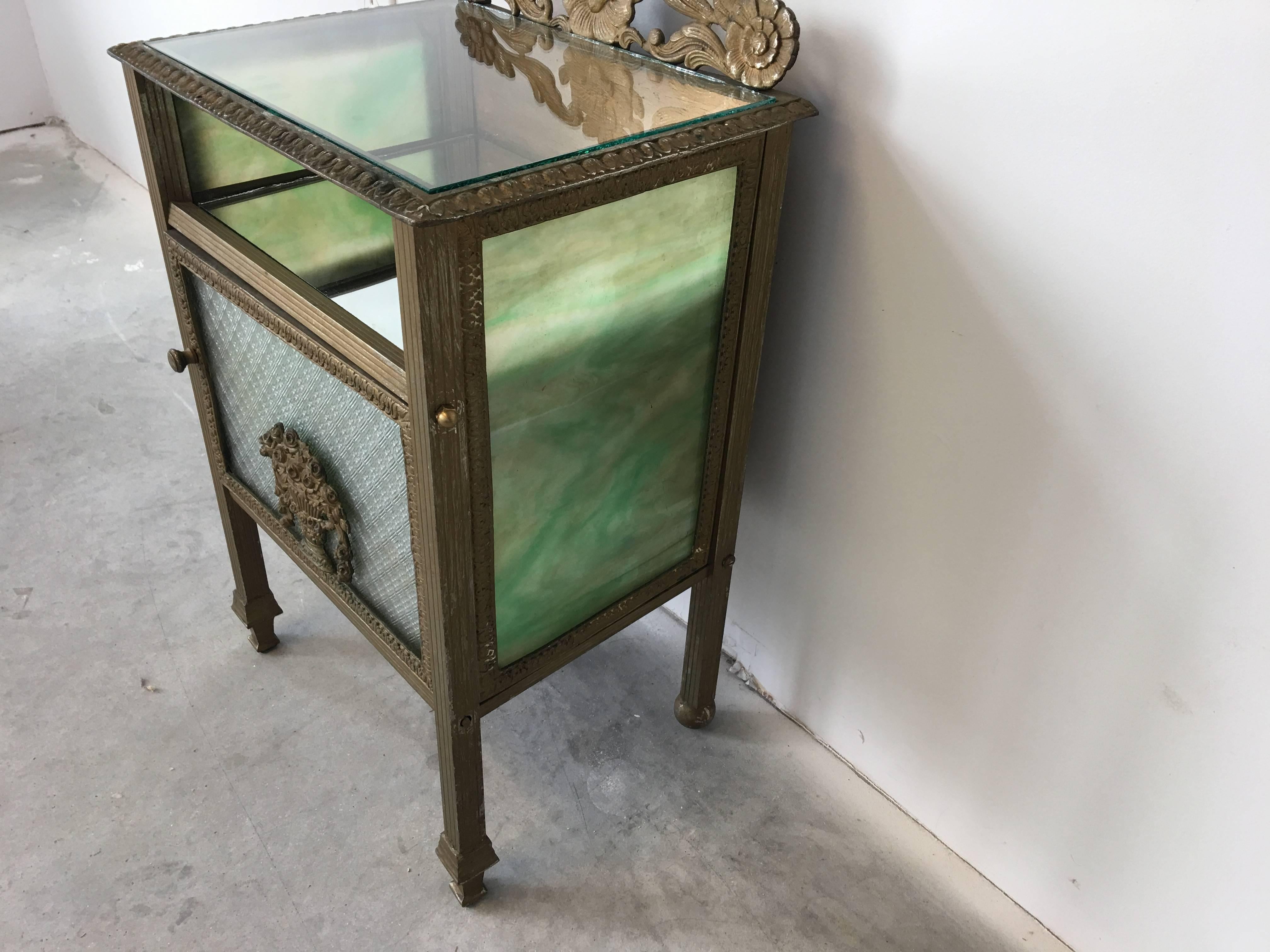 Offered is a gorgeous, 19th century Art Nouveau slag glass, bronze, and metal side table. This petite piece is absolutely stunning, with a mirrored shelf, glass door, and giltwood backing. The slag glass is in pristine condition.