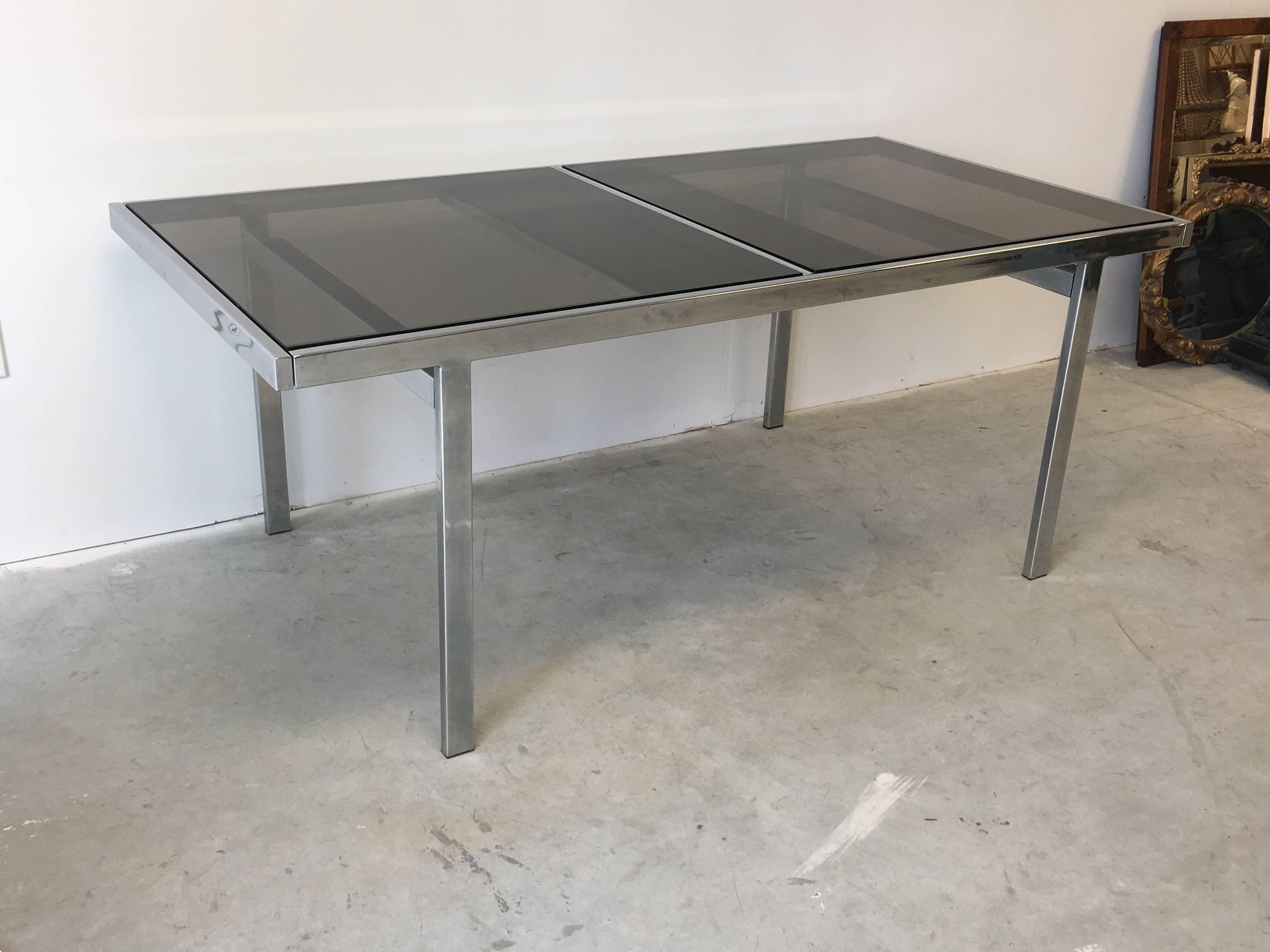 Offered is an absolutely stunning, Mid-Century Modern 1970s Milo Baughman chrome dining table with three smoked glass panes. This table extends from both sides, revealing a centre extension. Pull on each side to reveal the centre, which simply lifts