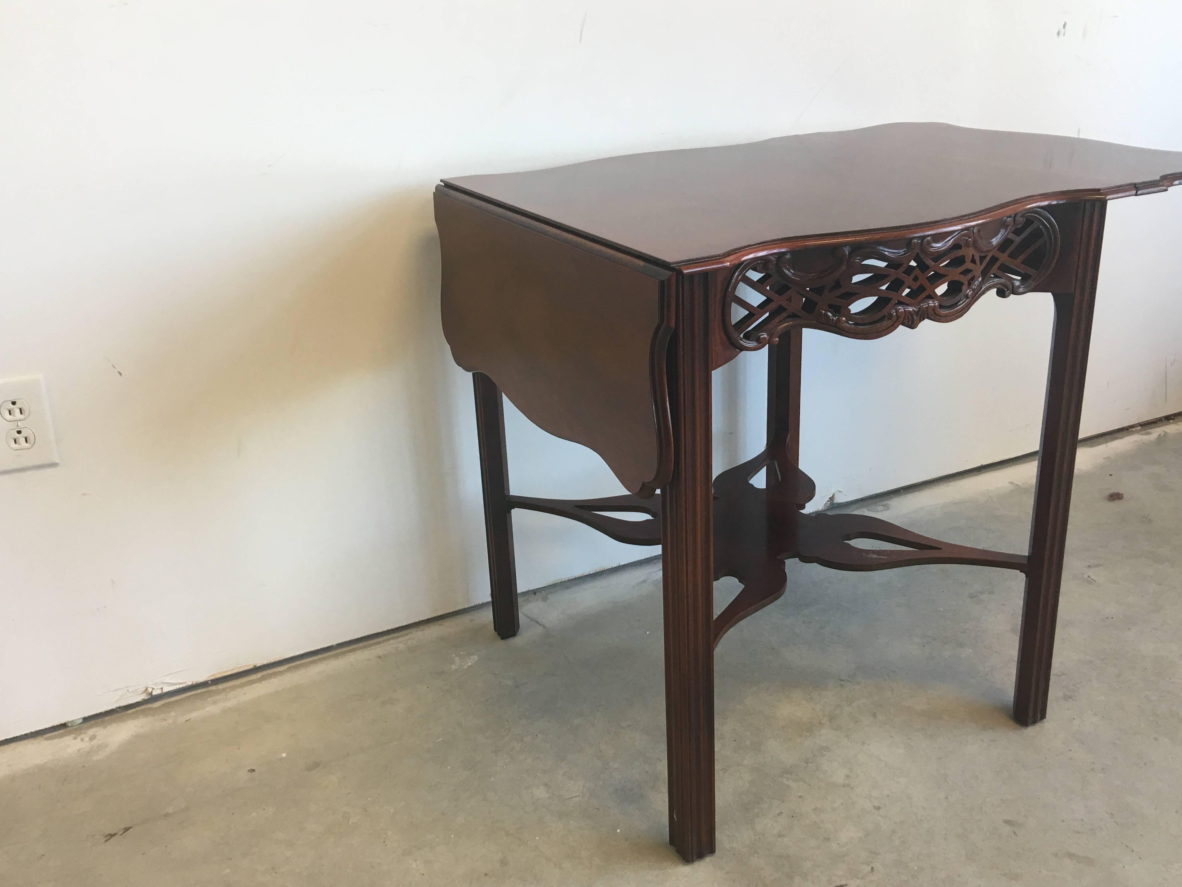 Offered is a stunning, 1960s Baker Furniture mahogany drop-leaf table tea table. Featuring drop-leaf sides and a serpentine top with intricately carved open fretwork frieze. Supported by straight chamfered legs and joined by butterfly stretchers.
