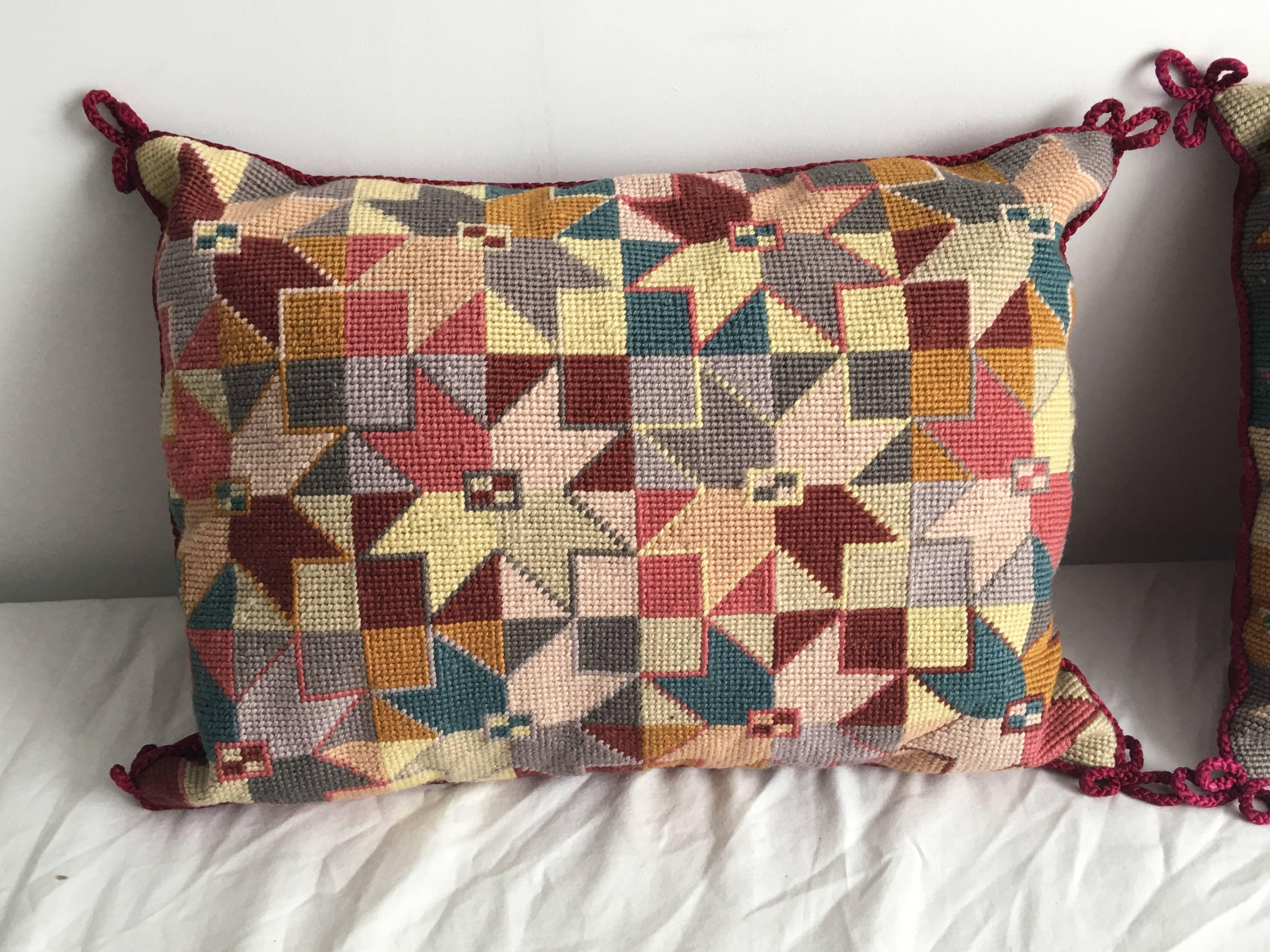 Offered is a gorgeous, pair of 1960s geometric needlepoint pillows. Each pillow is accented with a pink rope-trim, red velvet backing and zipper. 

Insert pillow is a poly-blend. Suggested to be replaced with a down insert.