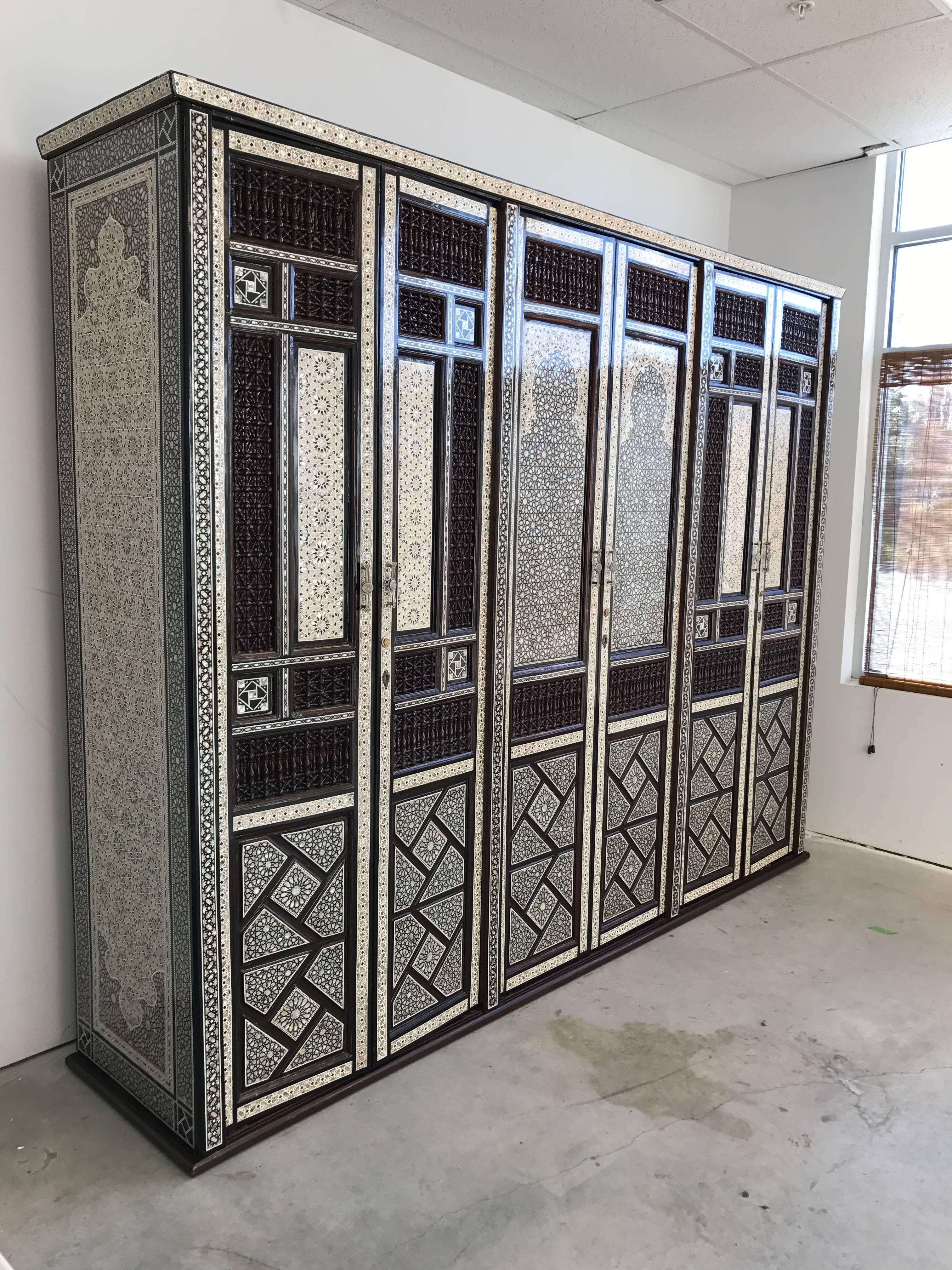 Offered is an absolutely stunning Middle Eastern armoire. The substantial piece is heavily decorated in a geometric and ornate pattern with mother-of-pearl and bone inlay, covered in a thick lacquer. Each set of doors open to shelving. Two outer