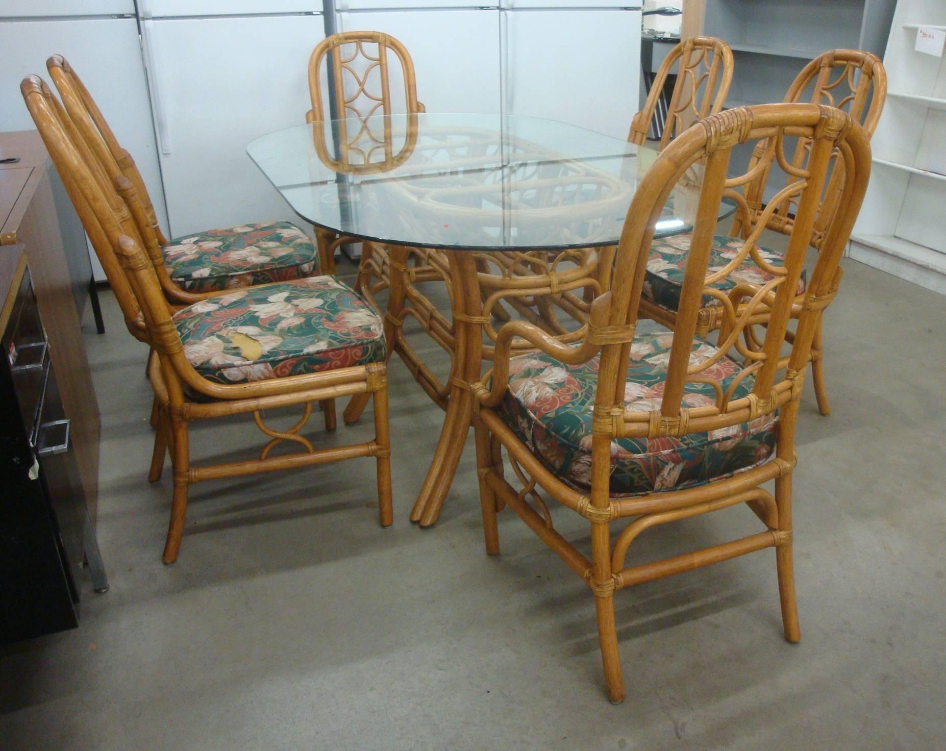 Offered is a fabulous, 1970s set of sturdy rattan McGuire or Ficks Reed style dining set. Stunning leather wrapped joints and curving trellis style details in the chair backs and skirts. Includes four side chairs, and two armchairs. Oval glass top