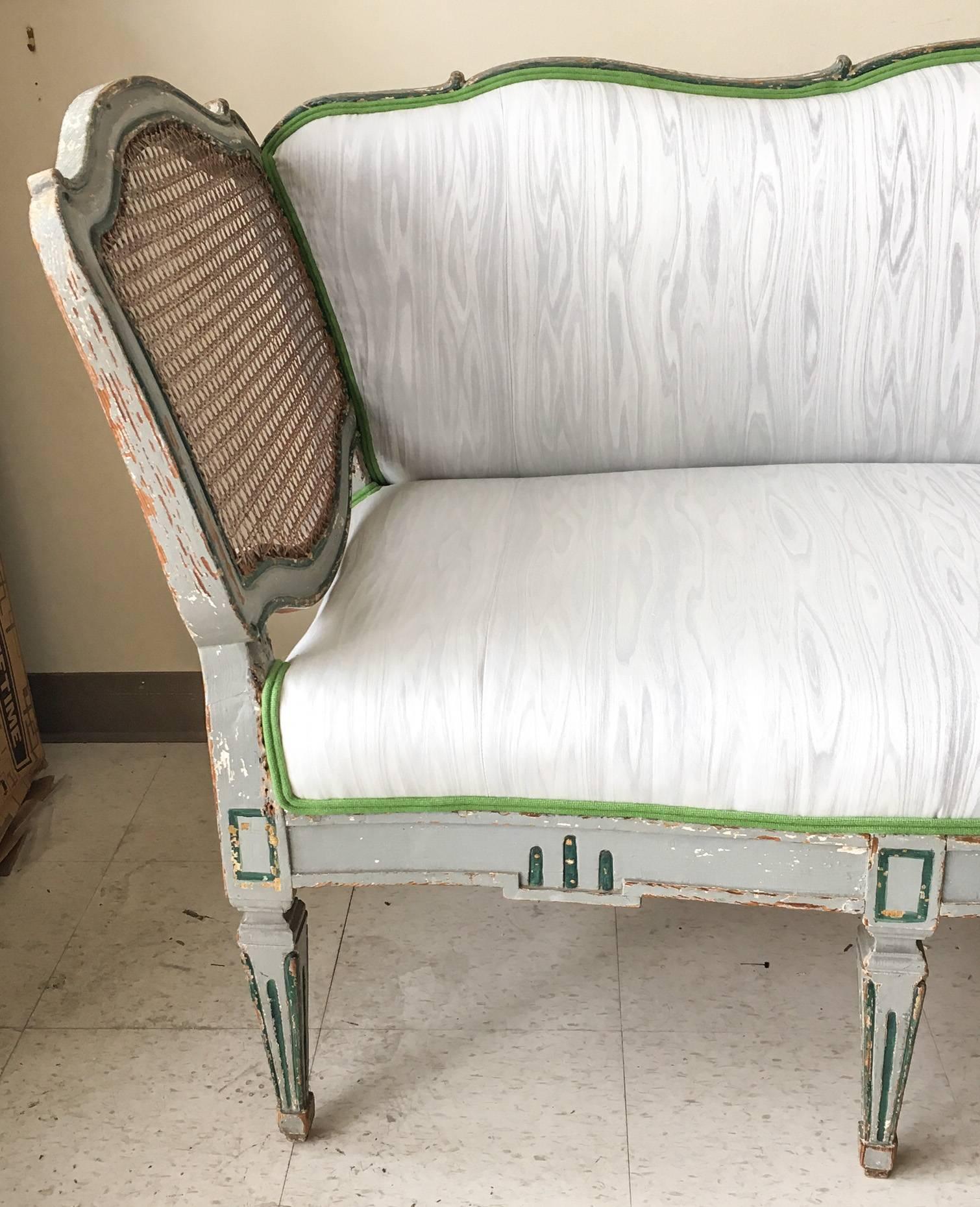 Offered is an elegant sculptural distressed wood and caned arm sofa dating to the mid-19th century, resting on eight spade-shaped legs and painted in soft grey, accented in deep green with traces of white. Purchased from the current owner of