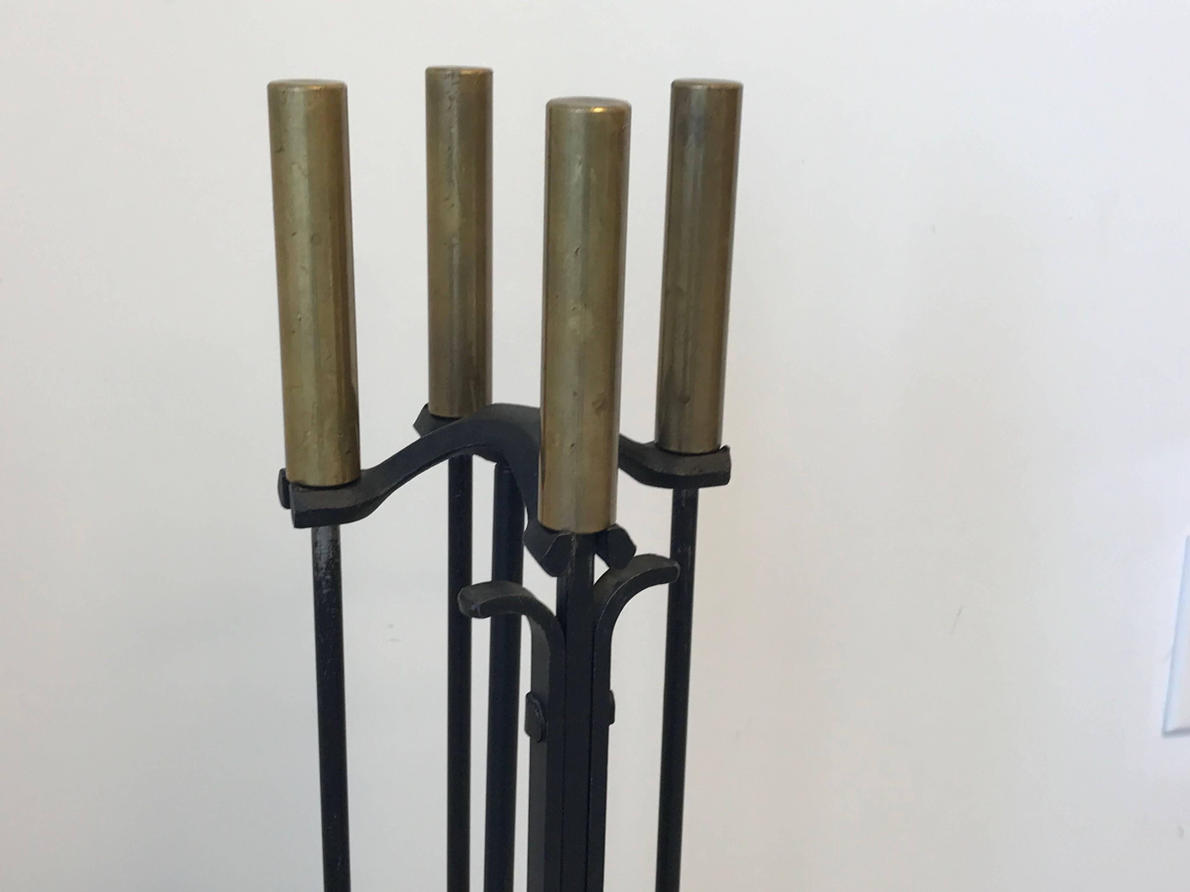 Offered is a gorgeous, 1970s modern Pilgrim iron fireplace tool set with cylindrical brass handles. Set of five; includes brush, poker, tongs, shovel, and stand.