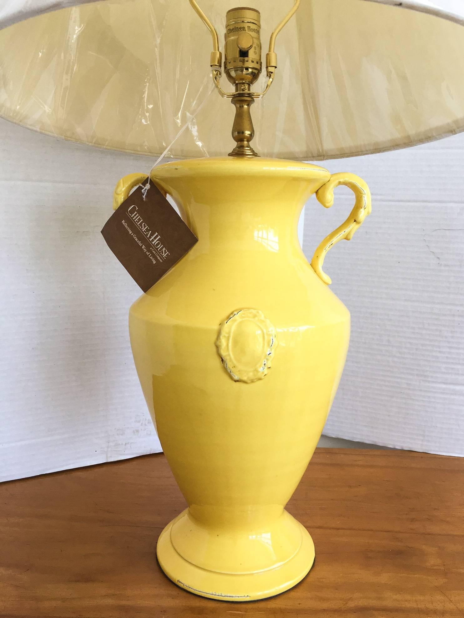Fantastic ceramic base table lamp by Chelsea House with two side handles and a cartouche decoration on the front and back. Lamp has some intentional distressing along the edges and comes with a new in plastic shade as shown. Never used. The lamp and