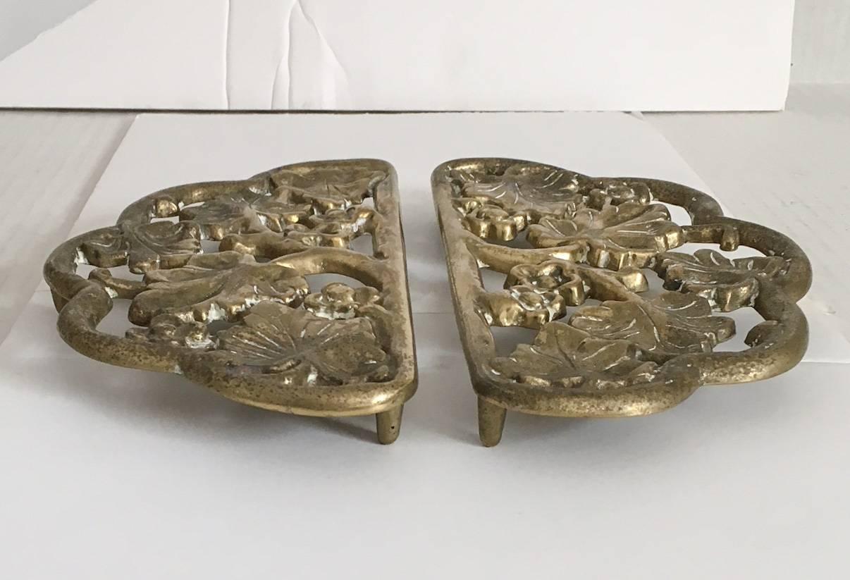 Offered are a pair of solid cast brass footed trivets by Harvin Metalworks (1930s) which later became the famed Virginia Metalcrafters. Trivets have a lovely scalloped edge and feature detailed ivy vine leaves and blossoms. Both are stamped on the