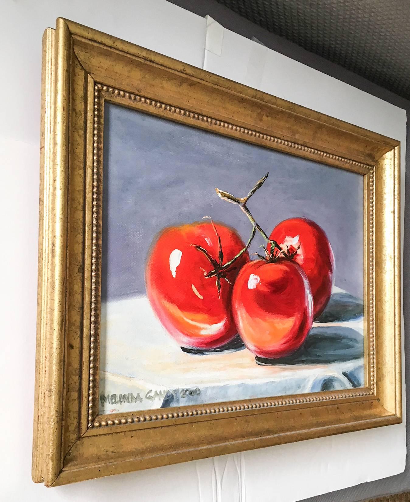 Delightful acrylic on canvas painting of three red tomatoes attached to their stem on a tablecloth against a purple-grey background by artist Melinda Gandy, 2000. Professionally framed in an Italian gilded popular wood frame with gold beaded detail.