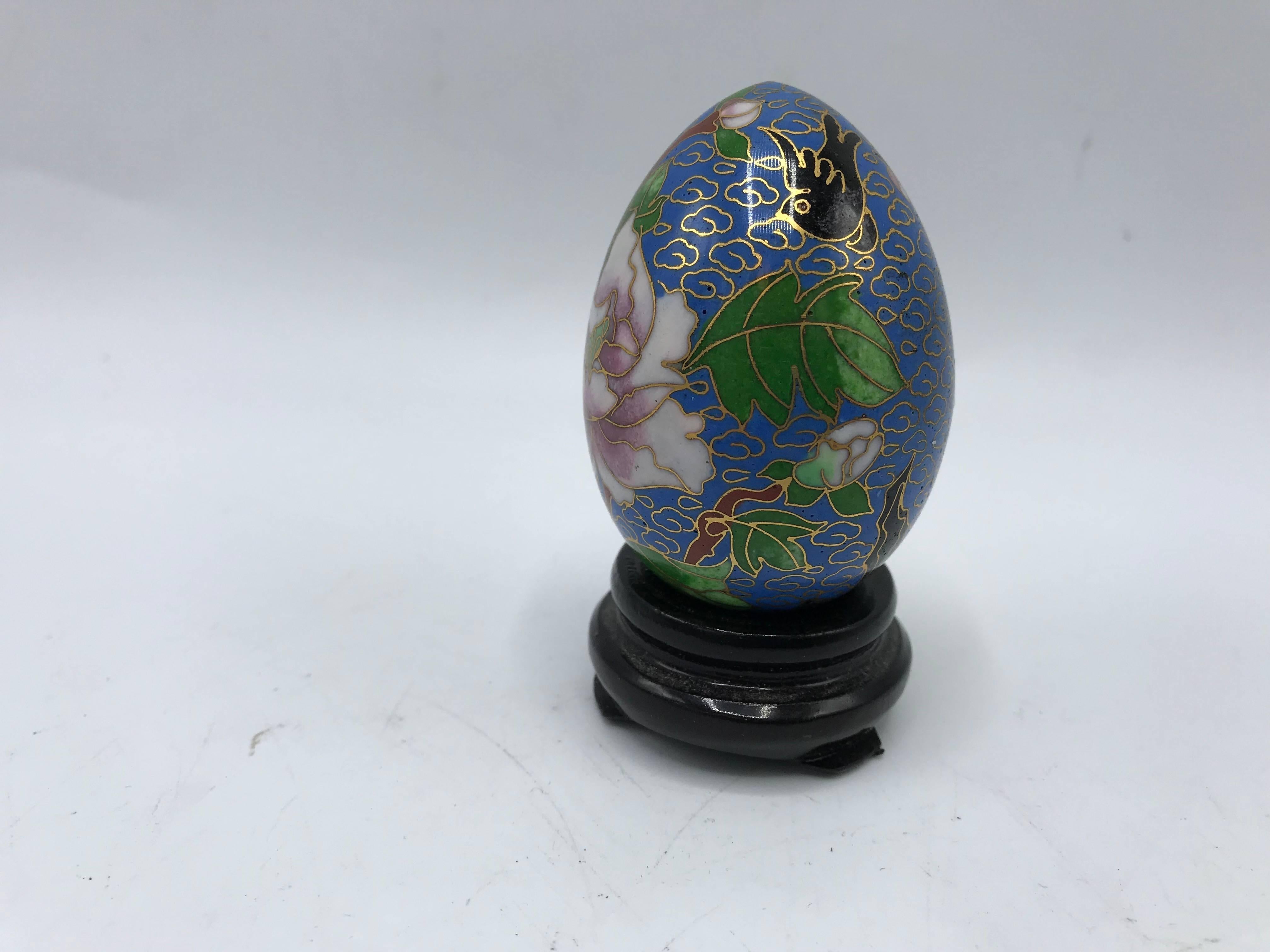 Listed is a fabulous, 1970s Chinoiserie Cloisonné egg sculpture on a decorative wood stand. The piece is primarily blue, with a white, green, pink, and black floral motif.
