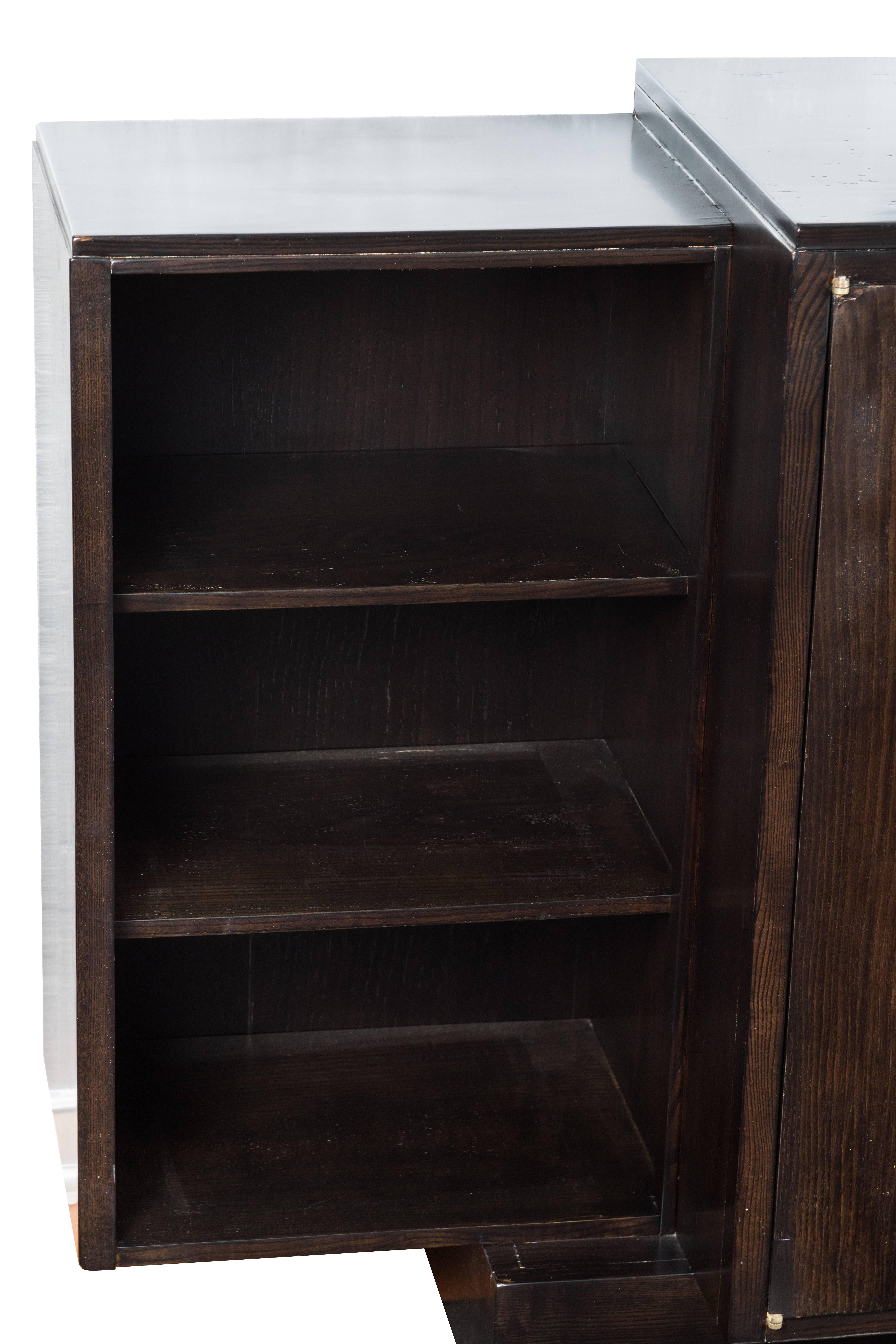 This vintage cabinet was designed by Émile-Jacques Ruhlmann. It is crafted from dark ebonized wood that houses spacious shelves and drawers behind doors.