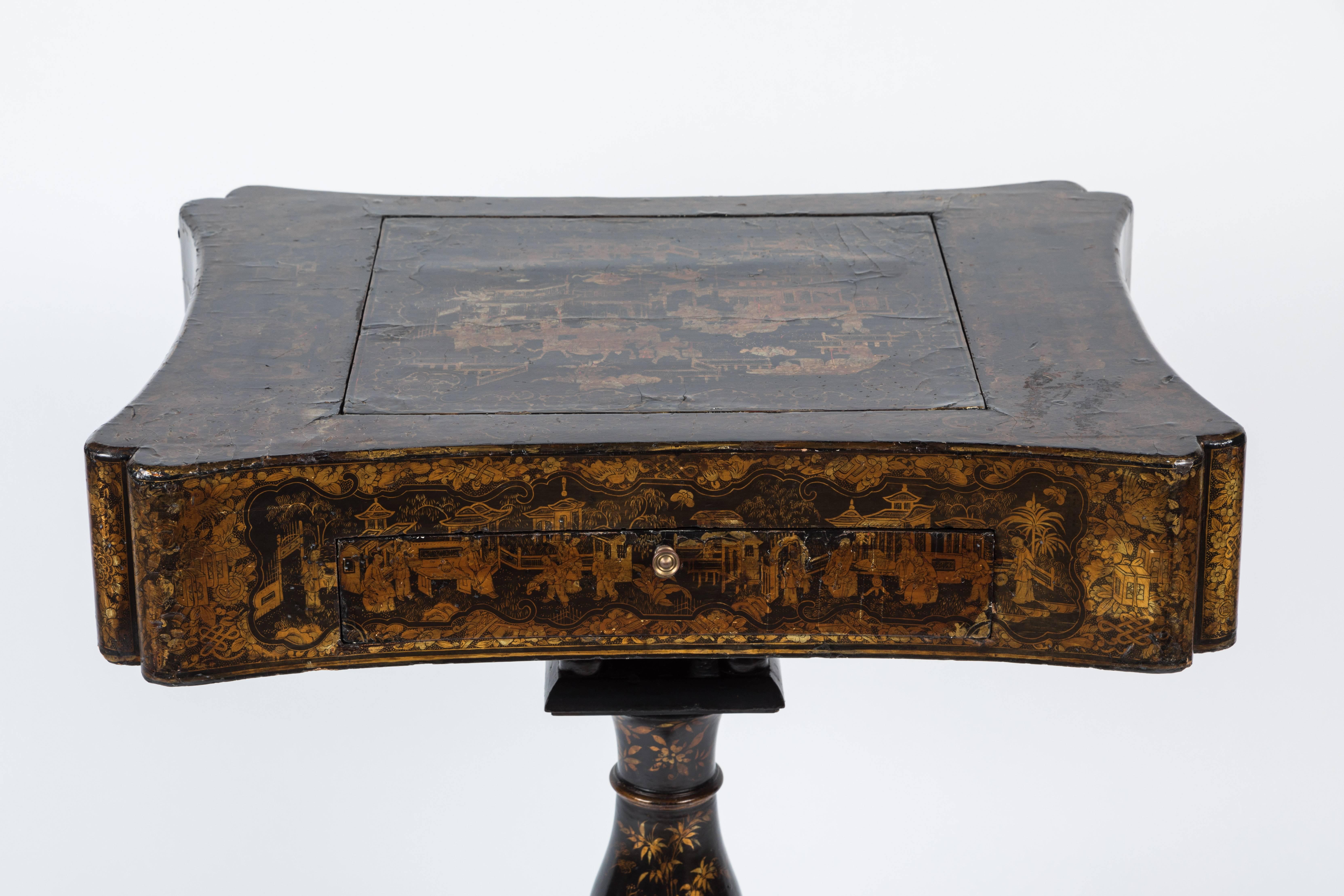 This antique English end table is rendered in the ornate Regency style. The entire pedestal design is made from lacquered wood decorated with gold-tone chinoiserie motifs. Smooth and polished, the top flips open to reveal various game boards.