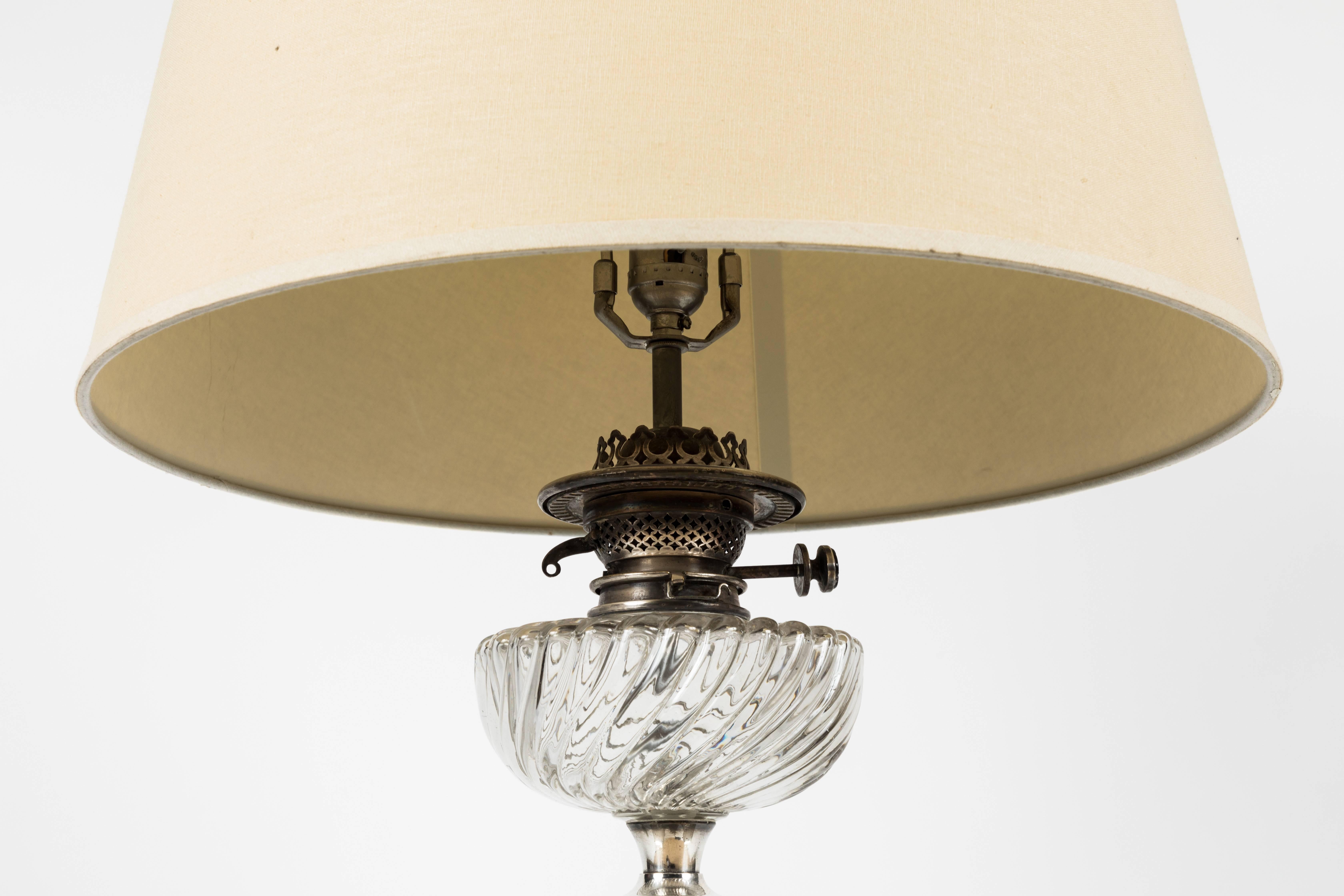 Antique English oil lamp, converted to electrical table lamp. Corinthian fluted column with glass. Silver plated brass with stepped detail around base. Recently electrified with three-way in line switch and custom made paper shade included. 