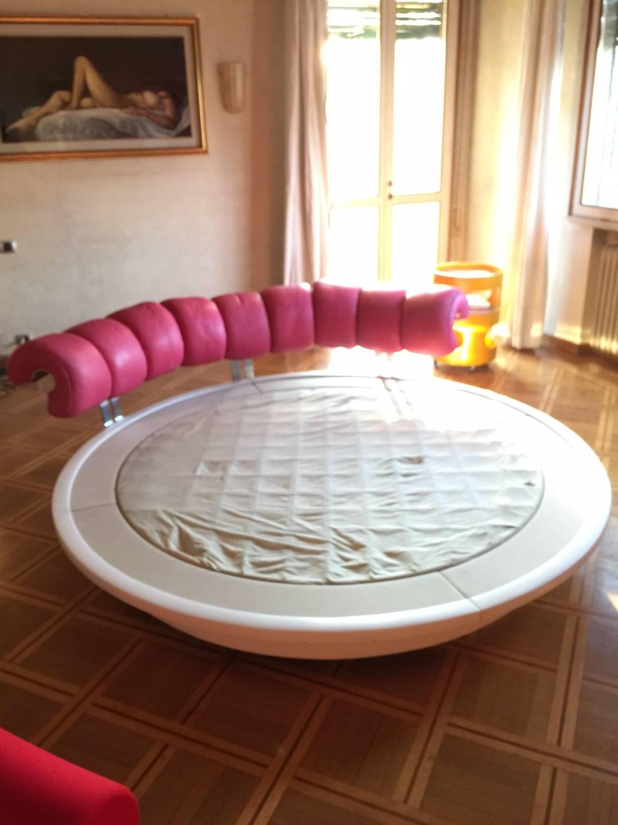 Rotating 360 round bed designed in 1967 by Luigi Massoni for Poltrona Frau. Very nice conditions, wear consistent with age and use. Swivel plywood white vinyl base, pink leather headboard. 