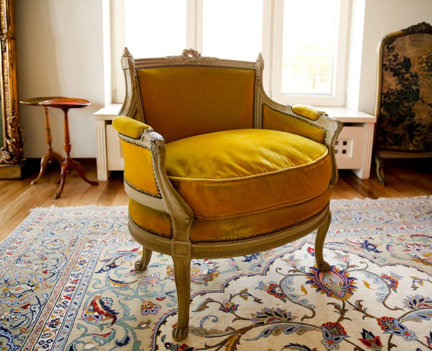 A masterfully carved 19th century Louis XVI painted marquise from France. The chair's frame is embellished with fantastic detailed carvings. The velvet mustard upholstery does show some wear and could be replaced. The carved frames wear antique