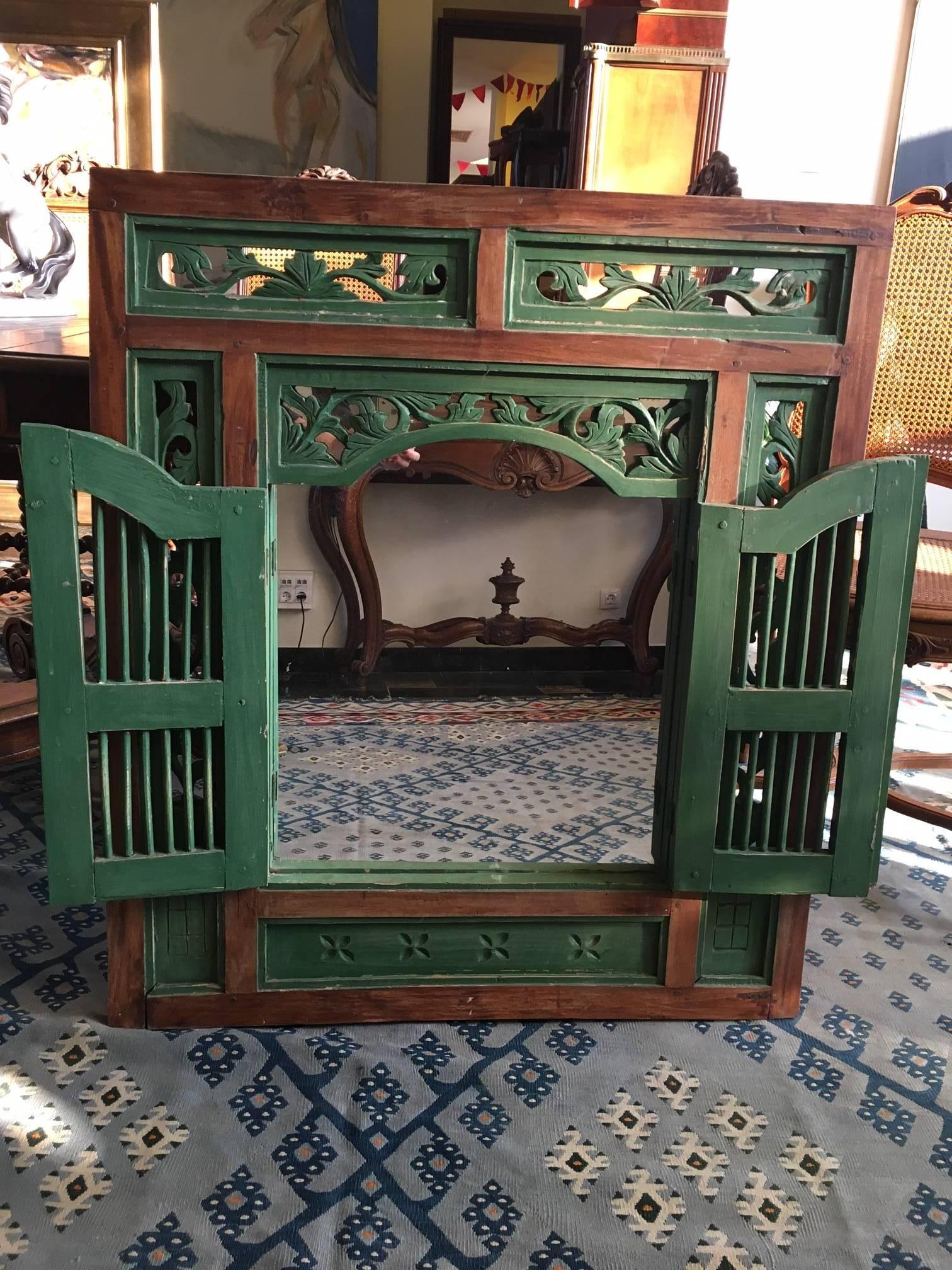 A mirror disguised behind a hand carved window frame, painted partially in dark green with antique finish.
Late 19th century.