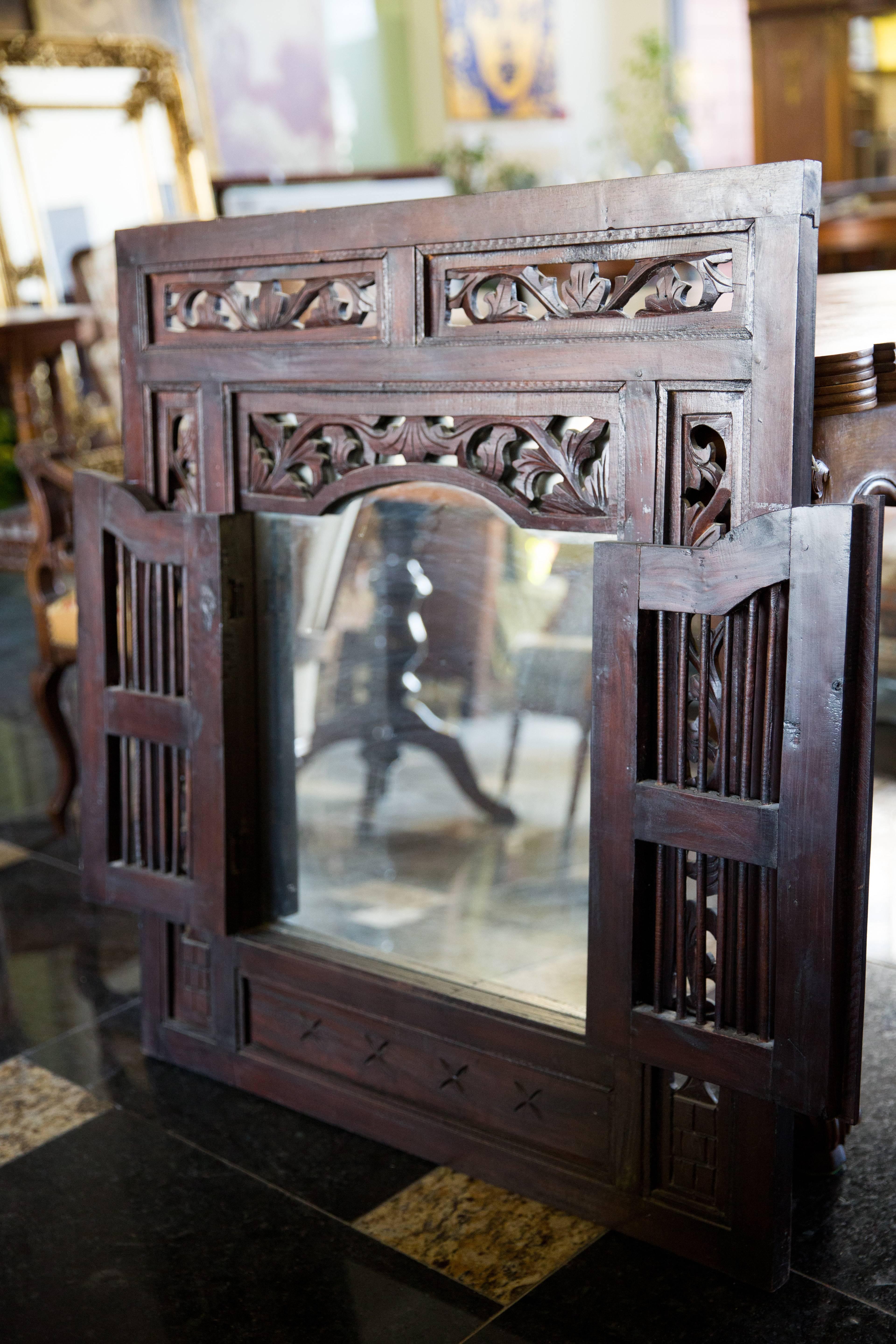 A mirror disguised behind a hand-carved window frame, in dark brown, 
late 19th century.