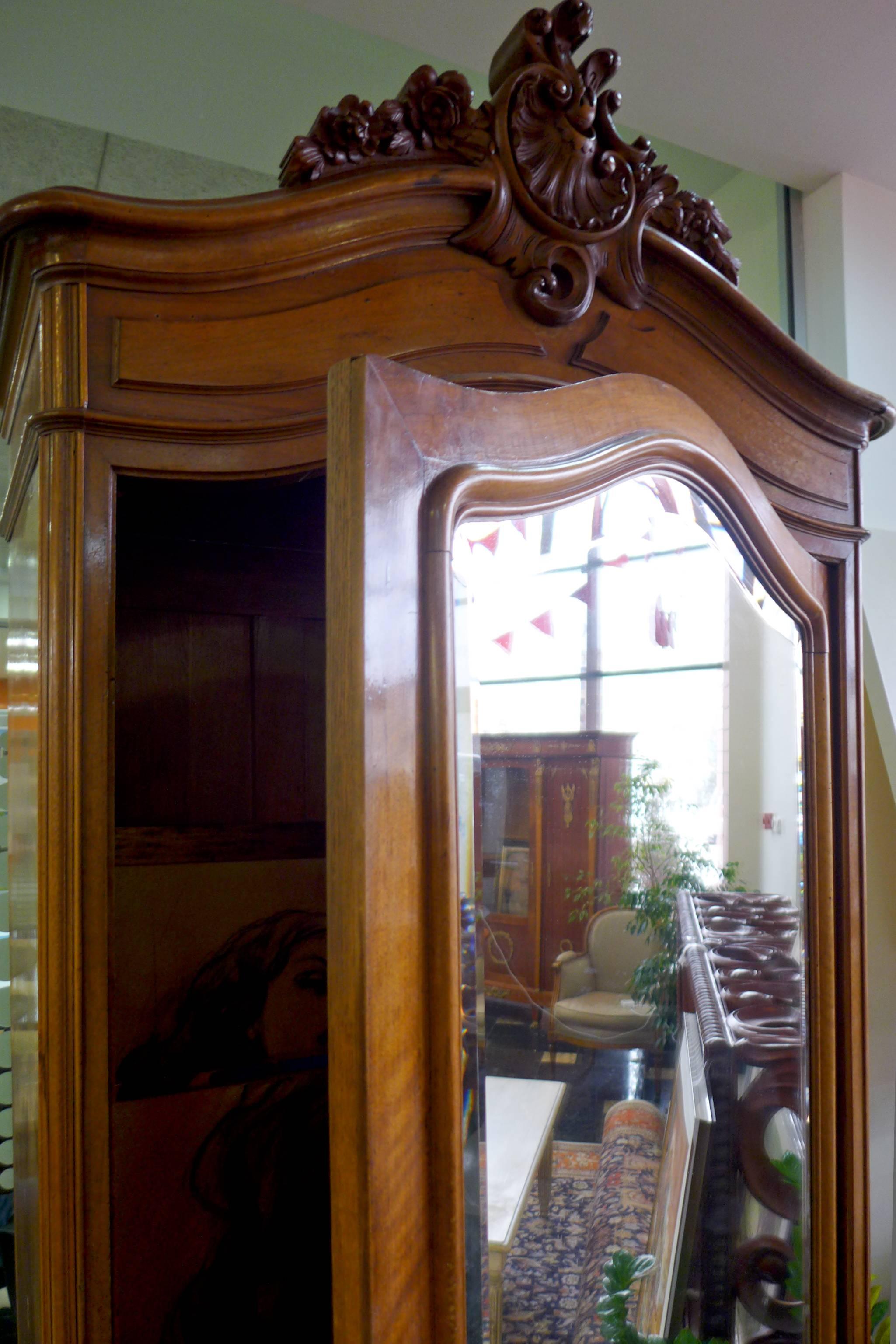 19th century French walnut cabinet/wardrobe with crystal mirror at the front door. The top has hand-carved leaves and flowers. It has three shelves inside. The cabinet is standing on small carved cabriole legs,
France, circa 1870.