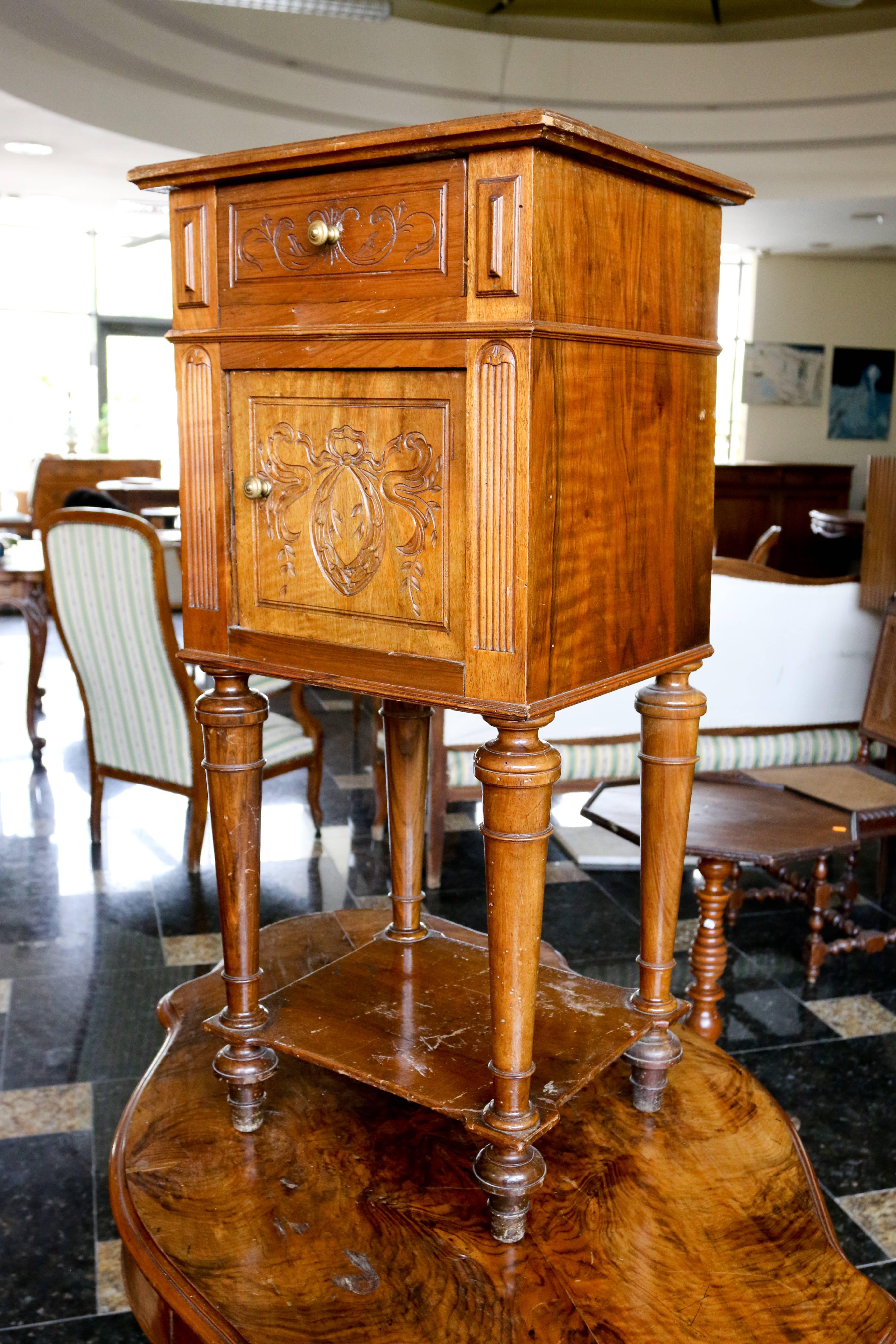 French 19th century walnut bedside cabinet. Often known as chevet or night table in France. The cabinet dates from circa 1880, it is made from walnut and it stands on tall turned legs. The drawer and the door have carvings in Louis XVI style