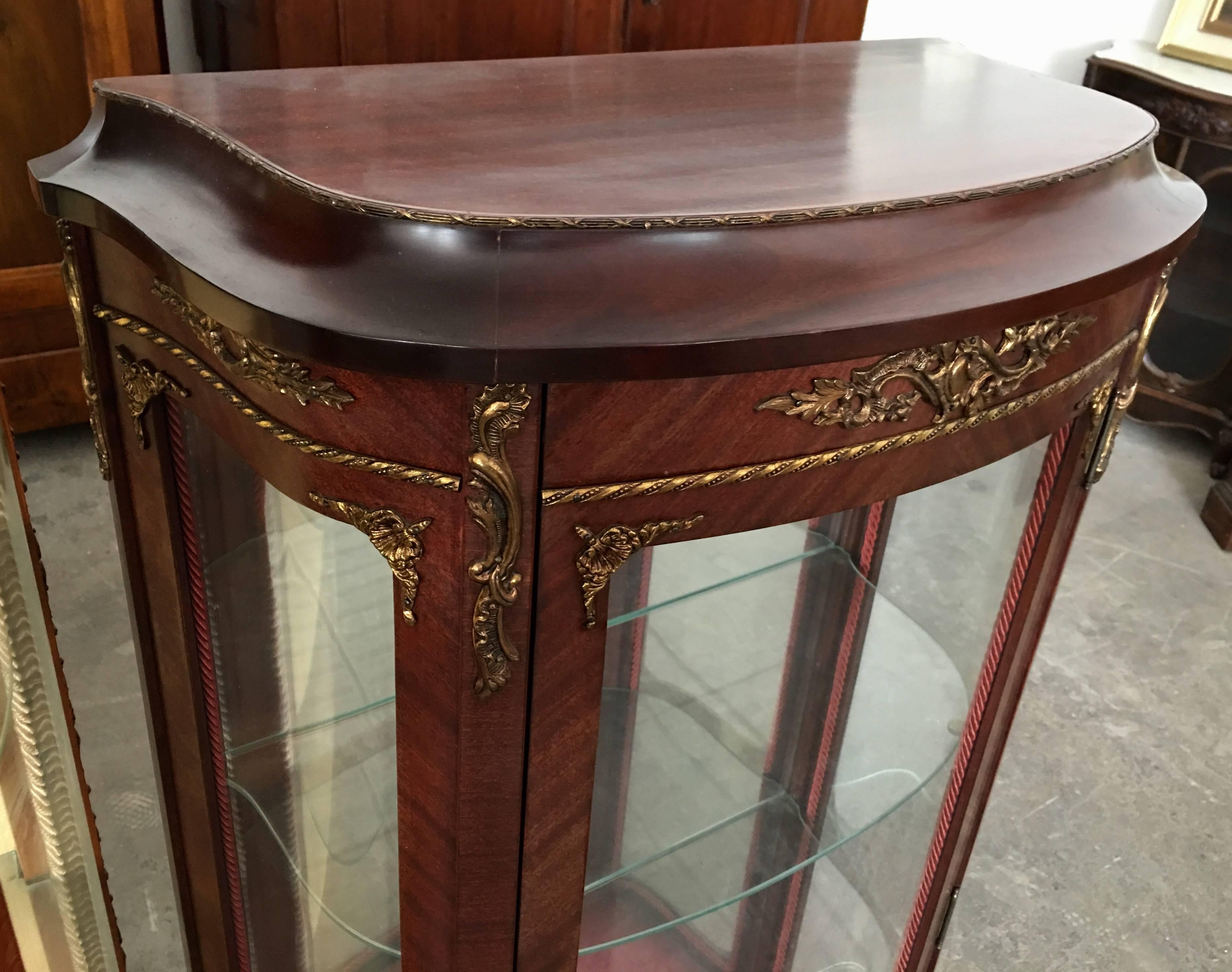 Antique French Louis XVI demilune vitrine
This 1900s antique French Louis XVI-style small demilune vitrine is made of mahogany wood with glass panels. Adorning the facade are brass ormolu accents of leafy and floral motifs and boarder trims with