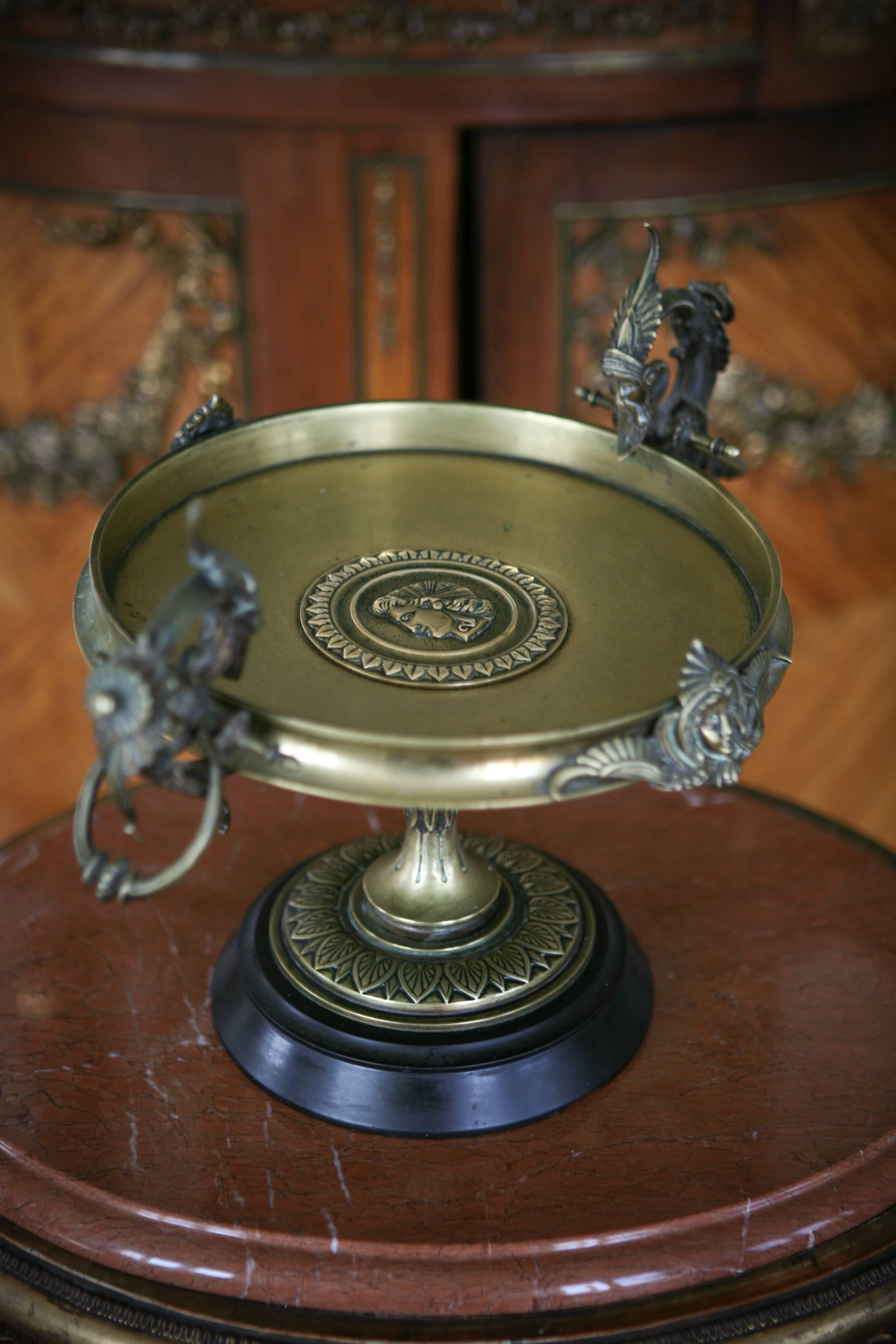 Large French bronze compote with two handles decorated with mask of men and two antique women's faces. There is an antique woman's profile at the center of the piece, which stands on a circular base made in black stone.
Work in the taste of F.