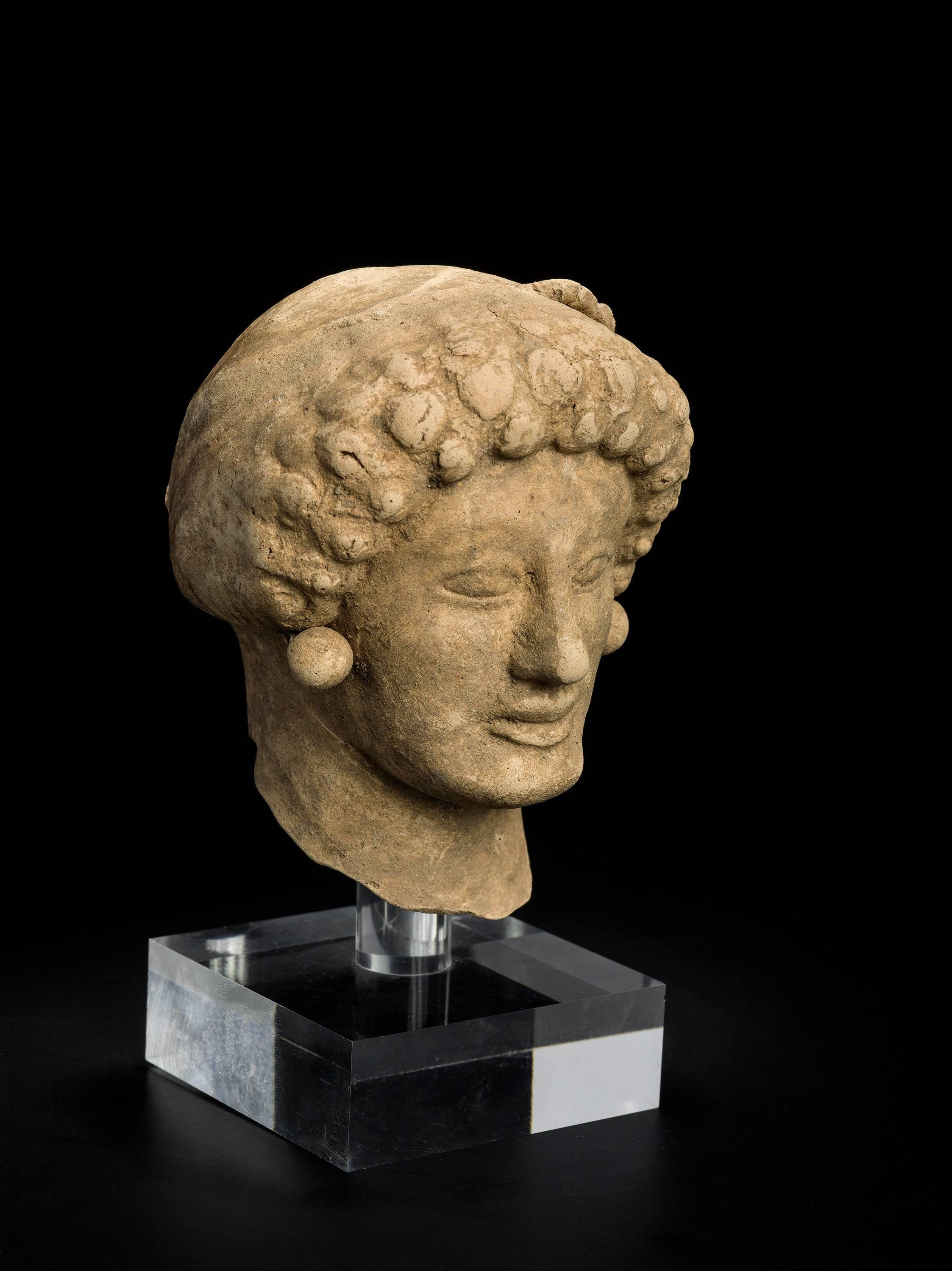 This votive head of a female is either depicting the donator or the sanctuary’s Goddess. The head originates from Medma, a ancient Greek colony in the Calabria peninsula, South Italy. The face is well modeled with almond shaped eyes and prominent