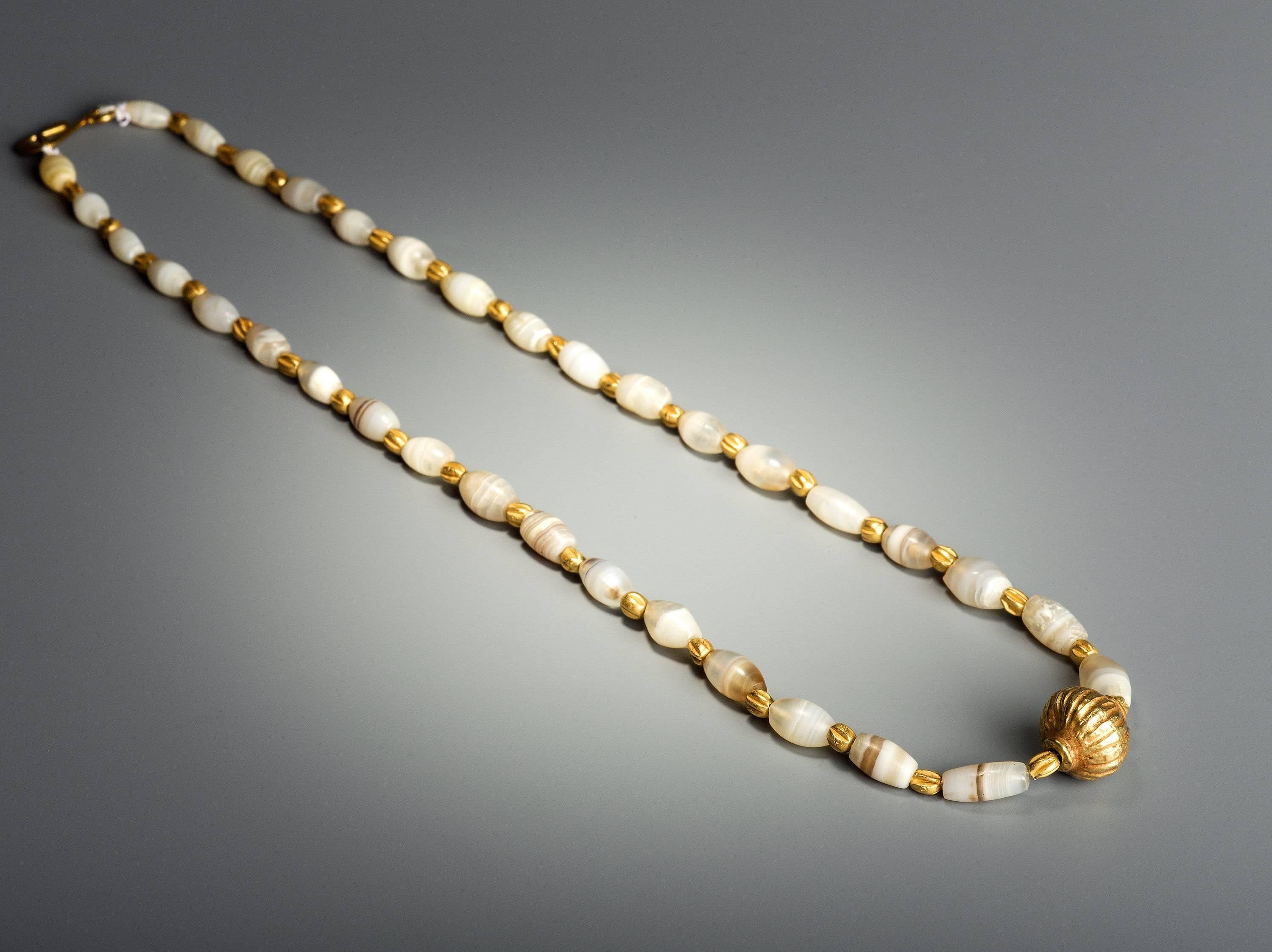 This elegant example of ancient jewellery is composed of opaque white and greyish brown agate beads interspersed with textured gold beads. The larger central gold bead is hollow and made from two halves. The necklace is restrung and the clasp is