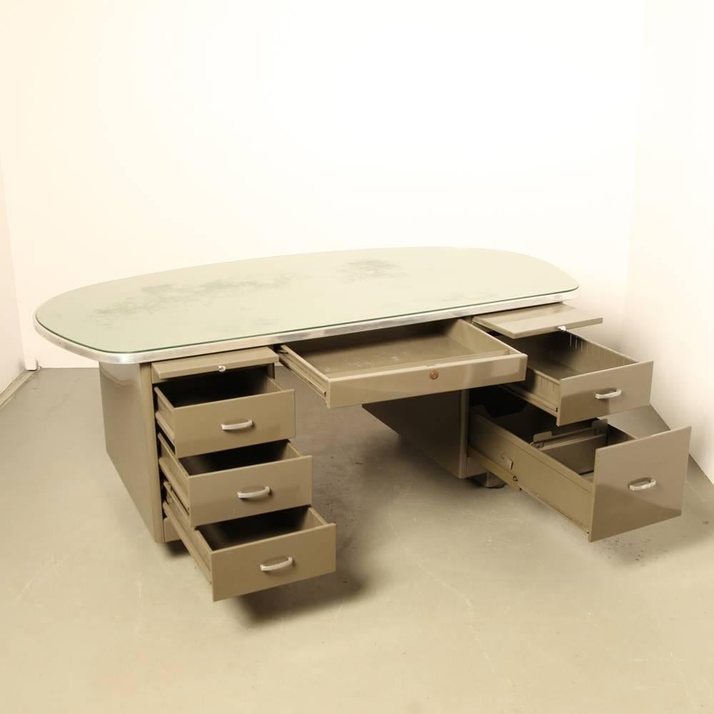 Label reads: “Ets VanderBorght Fres Bruxelles”

Desk made of sheet steel with two drawer blocks and a rounded top covered in green linoleum with a glass top and aluminum edging. Drawer block left with three low drawers; drawer block right with one