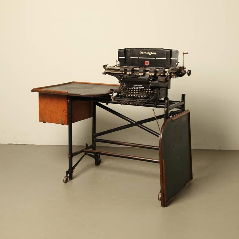 Remington typewriter with table on wheels.
Type: Remington vertical adder model 22.
The right part of the table can be removed or folded down.
Type writer can be removed.
Used in bankers world, vertical typing.
 
