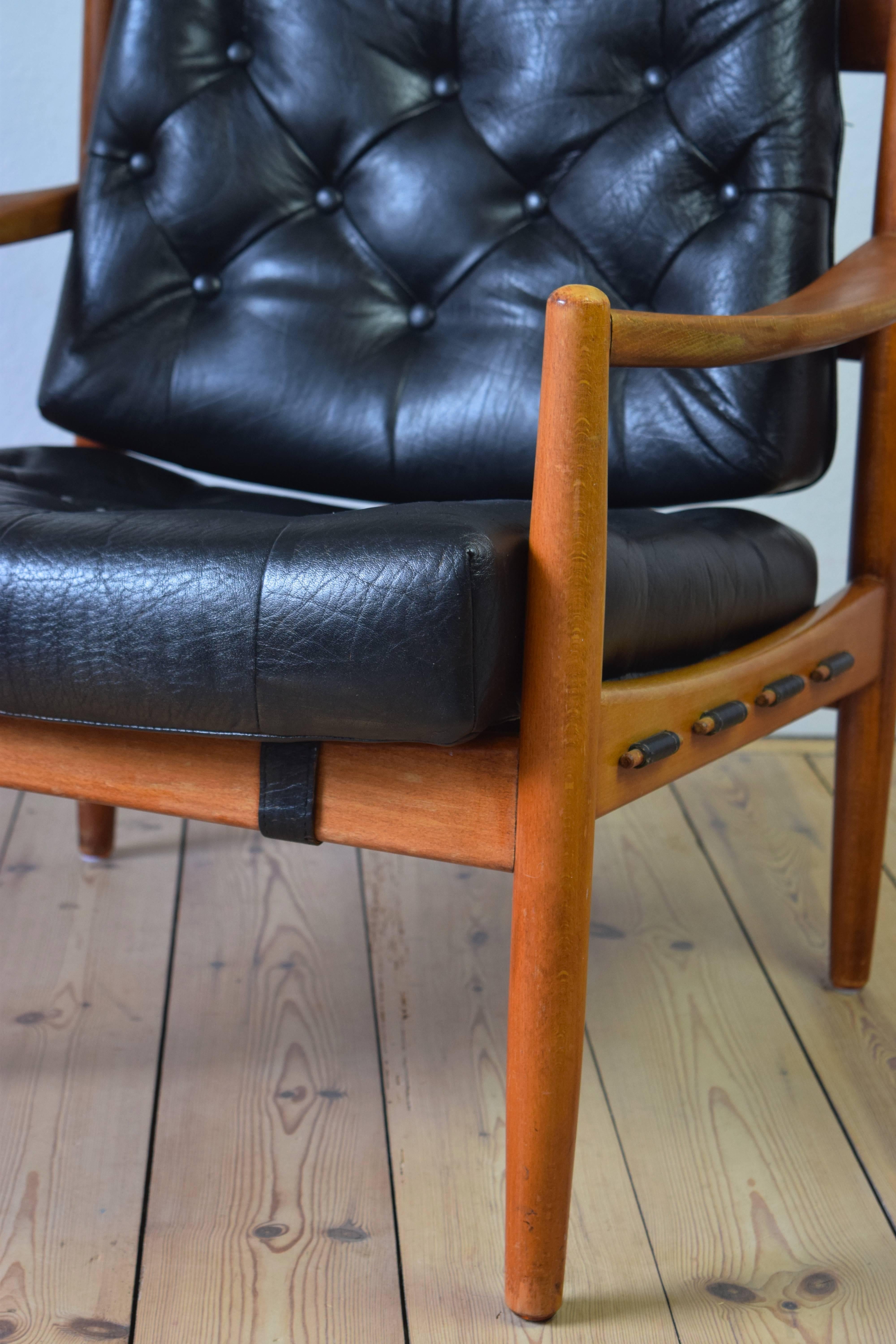 Stylish low-slung lounge chair in beech and leather from the 1960s. The seat cushion sits on a canvas harness which is hung from the frame and looped through and secured using wood stops. Both cushions are secured to the frame using straps. There