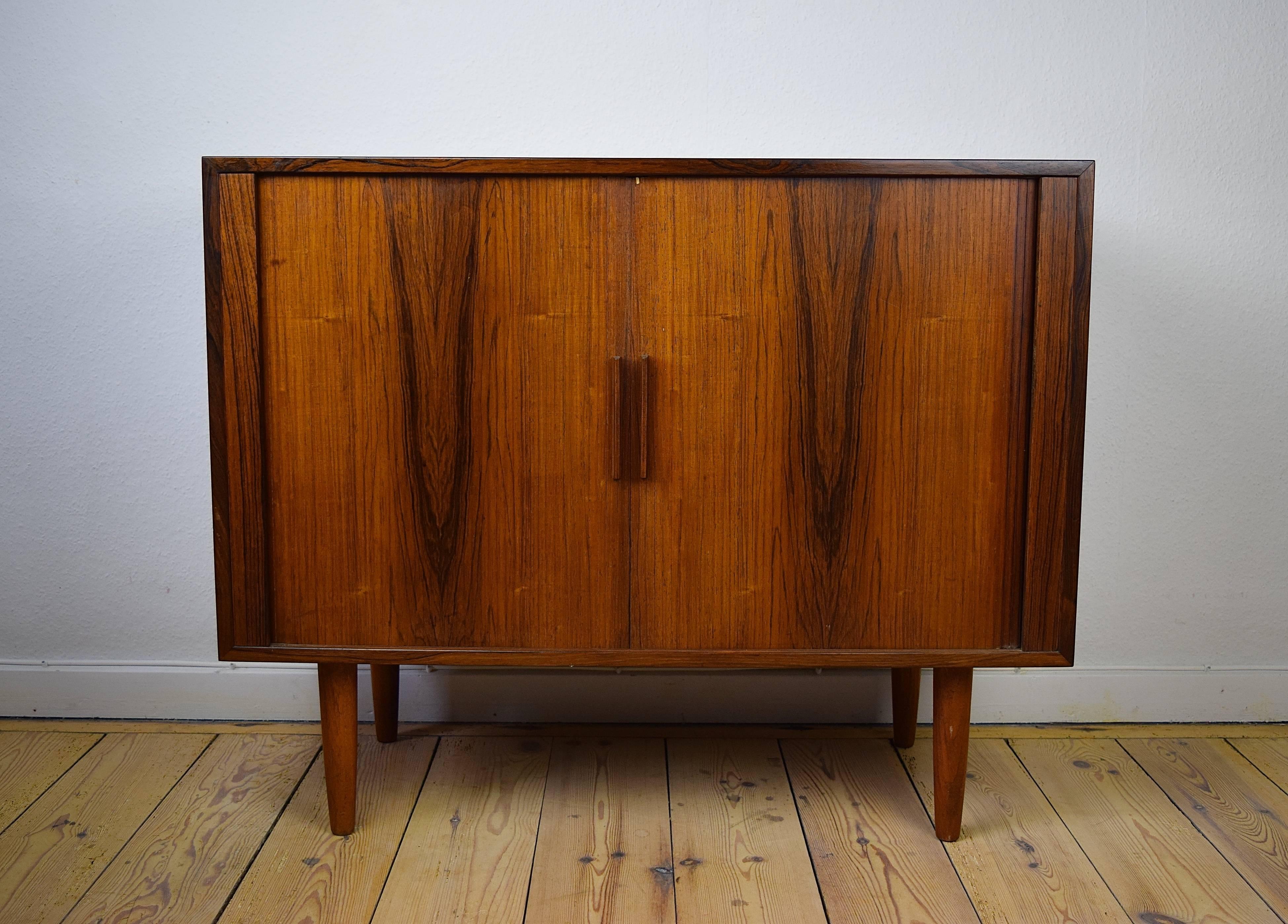 This rosewood cabinet was designed by Kai Kristiansen and manufactured in Denmark by Feldballes Møbelfabrik in 1960. It features tambour doors with two internal removable compartments and space for vinyl records.