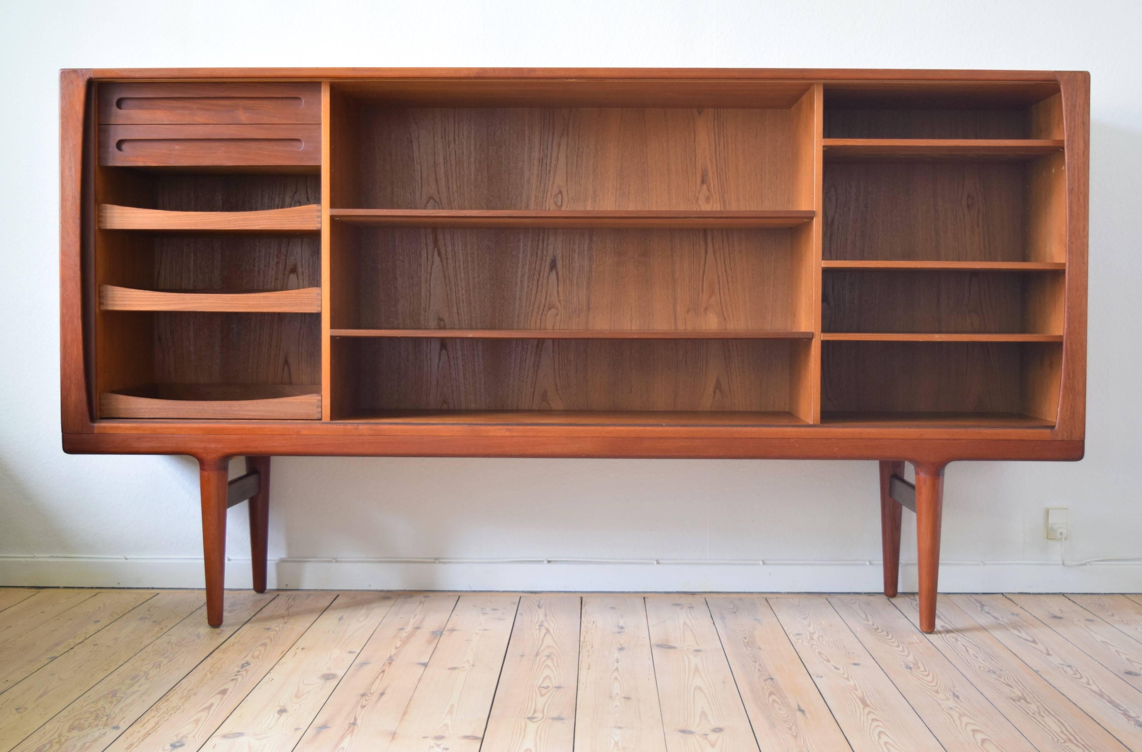 Danish high teak credenza from the 1960s featuring four sliding doors with matched teak grain, interior shelves and drawers. An elegant solid teak bevelled edge moulds in to elegant tapered legs. This item has been restored and is in a very good