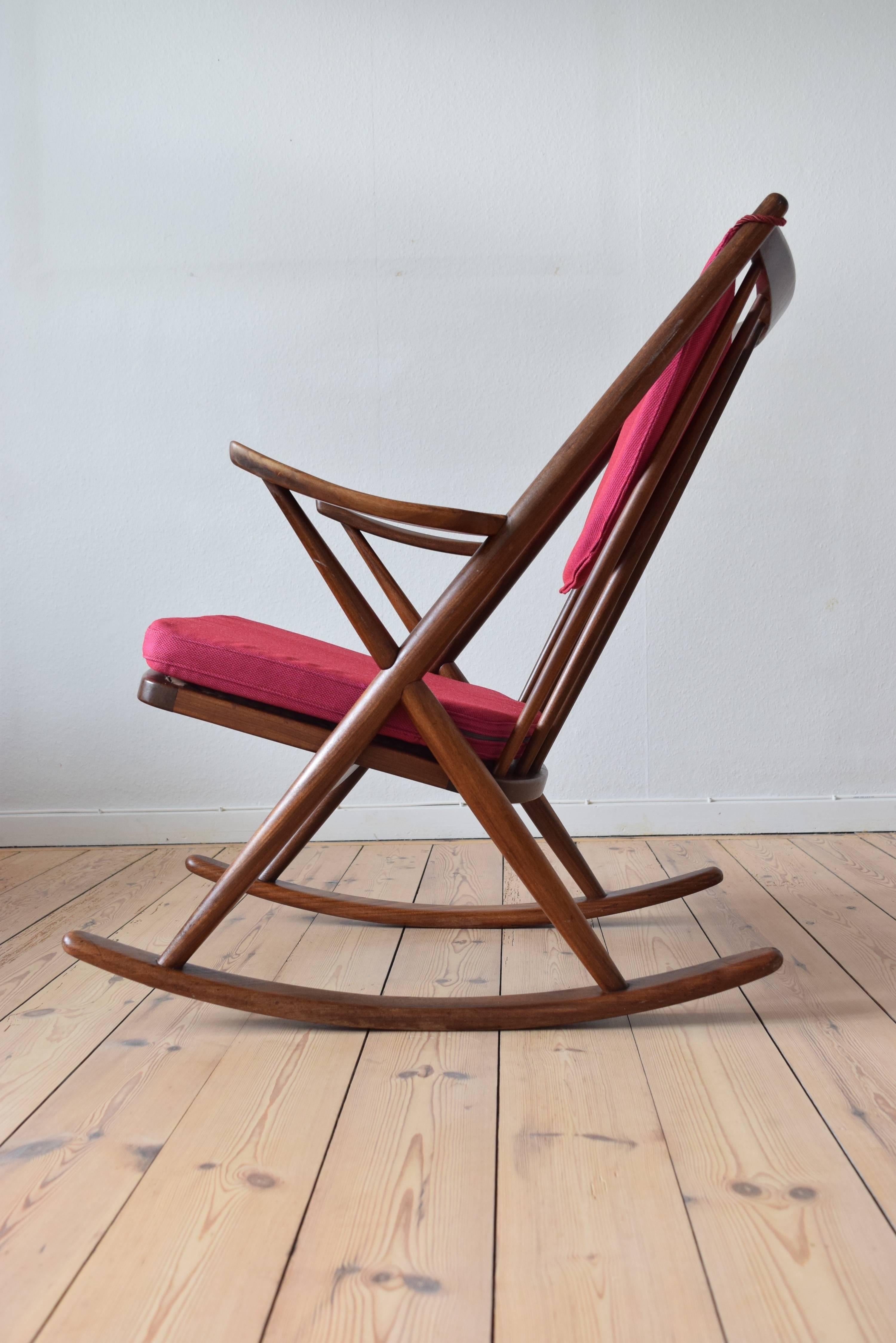 This Mid-Century Modern rocking chair was designed by Frank Reenskaug in 1958 and manufactured by Bramin Møbler in Denmark. It is built from solid African teak and features a crossed frame between the skids and slightly curved armrests and has been