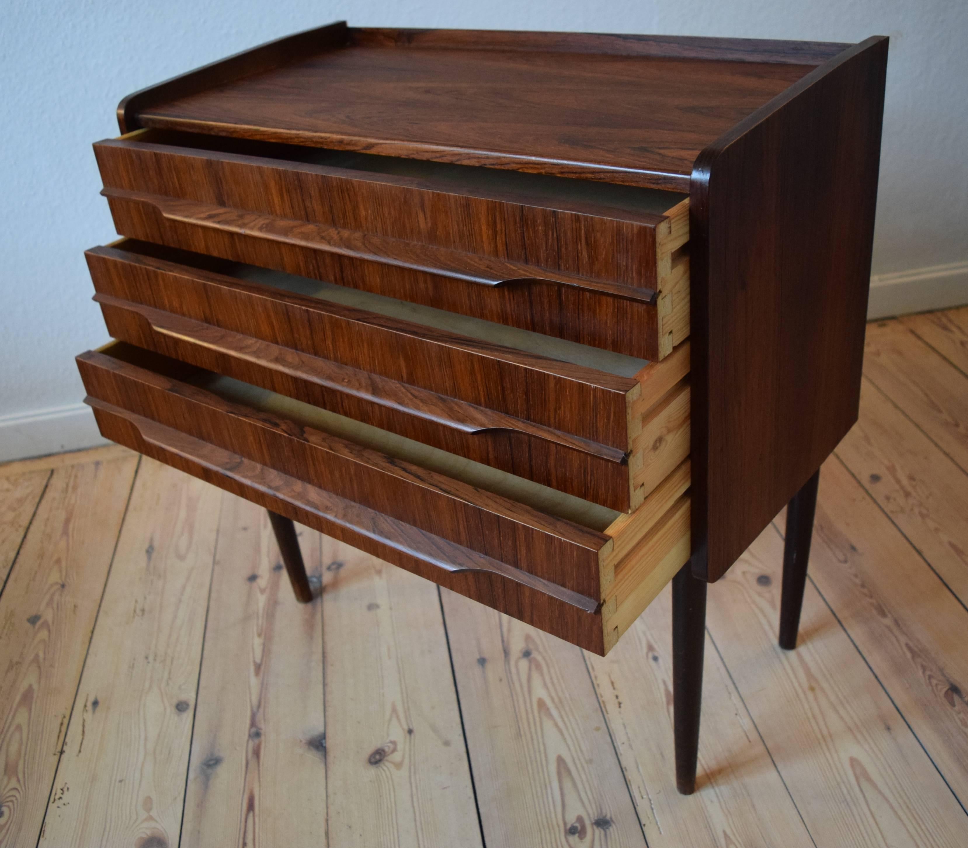 Small three-drawer entry chest, designed and manufactured in Denmark in the 1960s. Features rosewood full length handles and sits on a turned and tapered solid rosewood legs. Striking grain throughout.
  