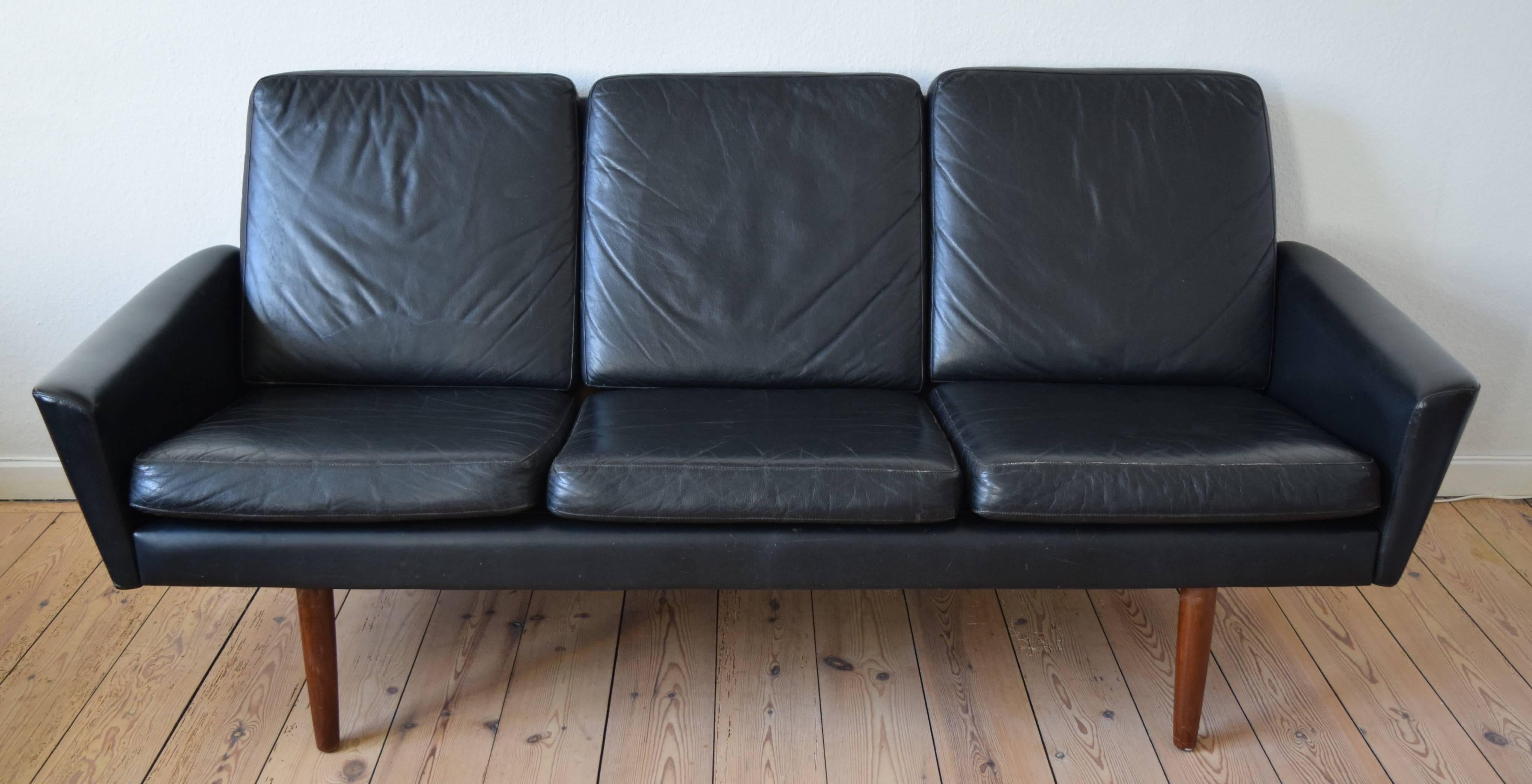 Leather three-person black sofa with teak legs manufactured in Denmark in the 1960s. The low slung design features angular lines and sits on solid teak legs. This is a genuine 1960s sofa in good condition with light wear for it's age. The sofa has
