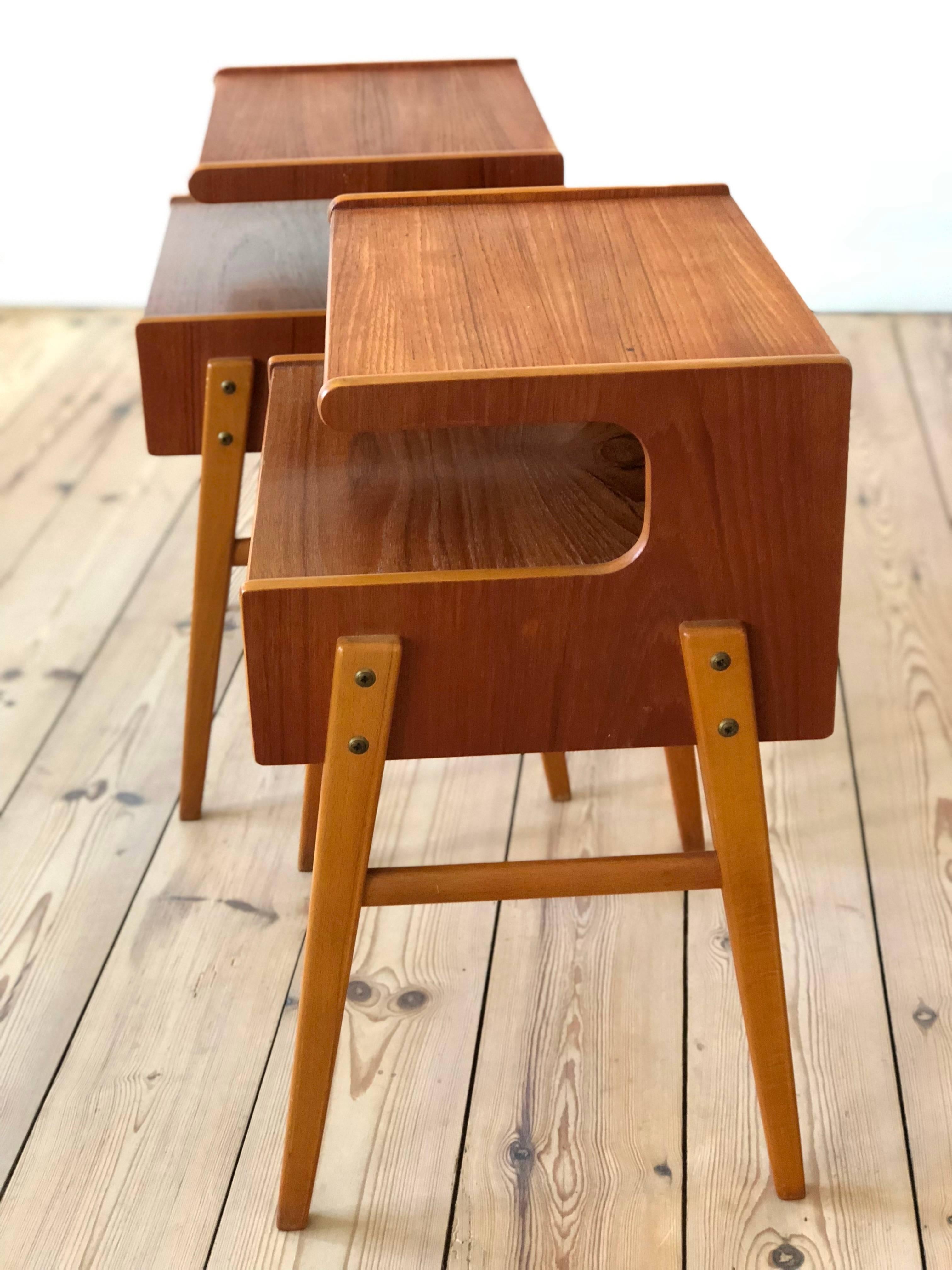 Teak and beech nightstands manufactured in Denmark in the 1960s. They each feature a drawer with shelf and top plate in a deep red teak hue. Sitting on beech frame base. Both these stands are in a very good vintage condition. Legs can be removed for