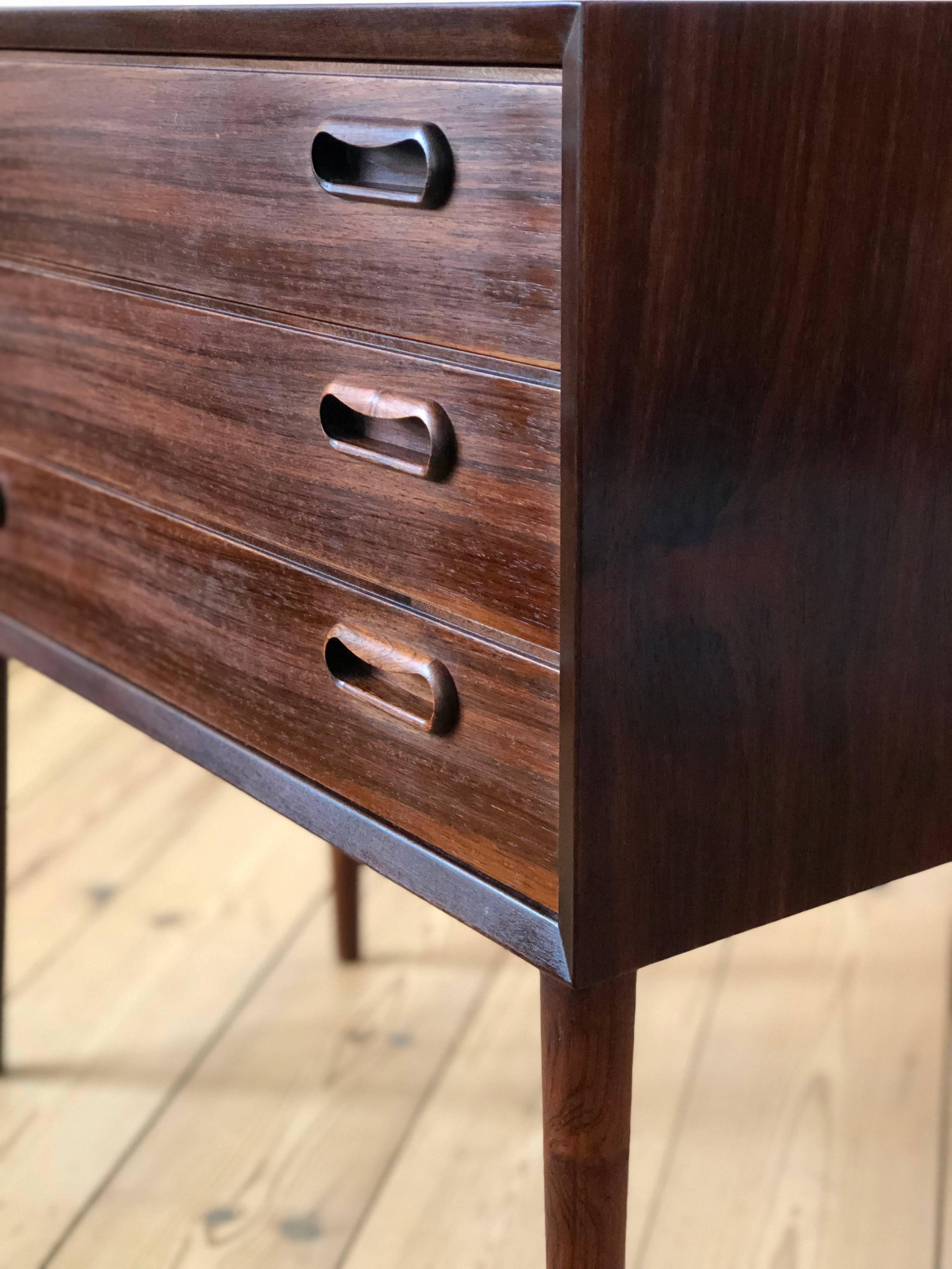 Small three-drawer entry chest, designed and manufactured in Denmark in the 1960s. Features inset rosewood handles and sits on a turned and tapered solid Brazilian rosewood legs. Striking grain throughout. Very few marks.