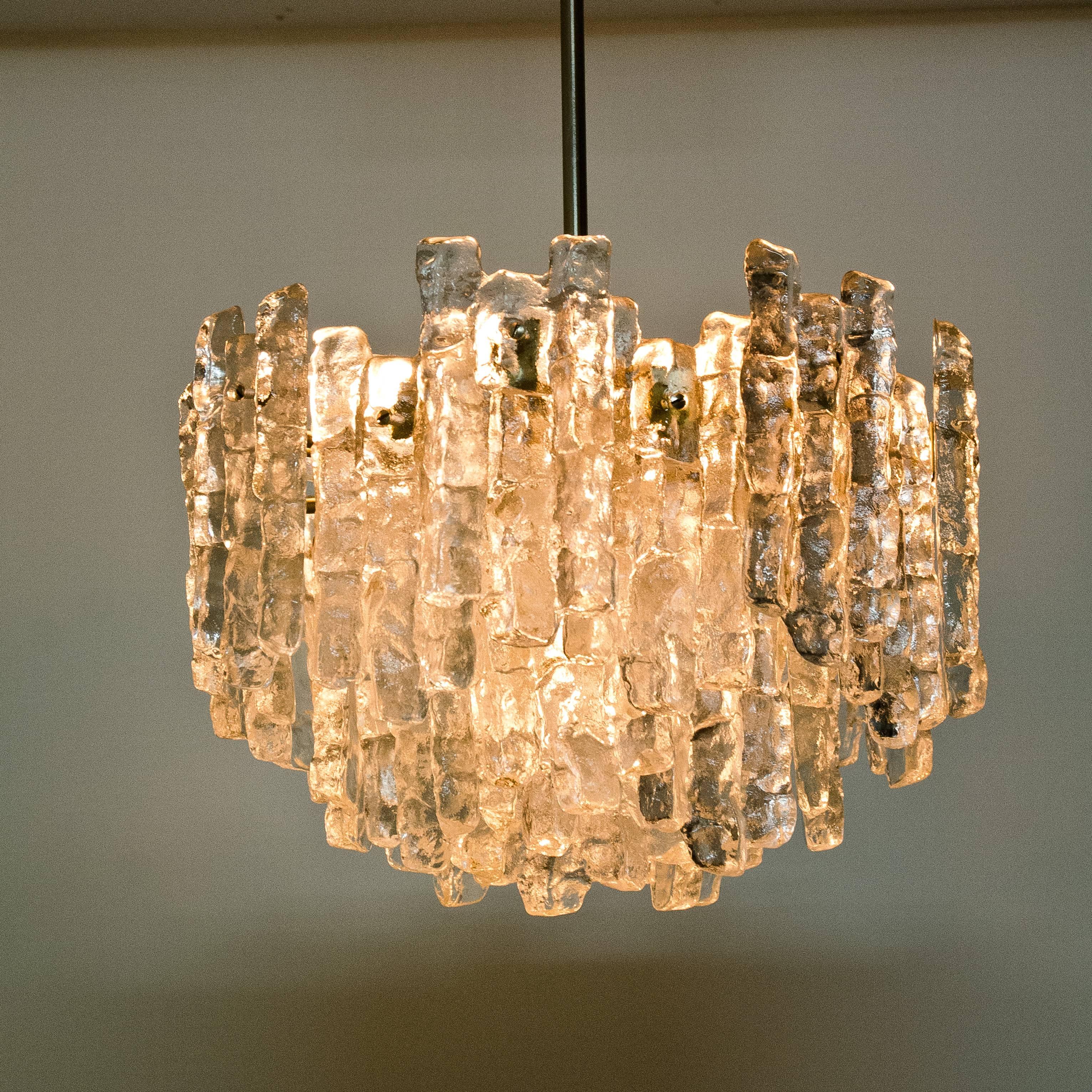 This modern chandeliers, manufactured by Kalmar Austria in the 1970s, have eight E27 sockets and three layers of textured solid ice glass sheets dangling from it. This unique chandeliers are not only functioning as light source but also as a