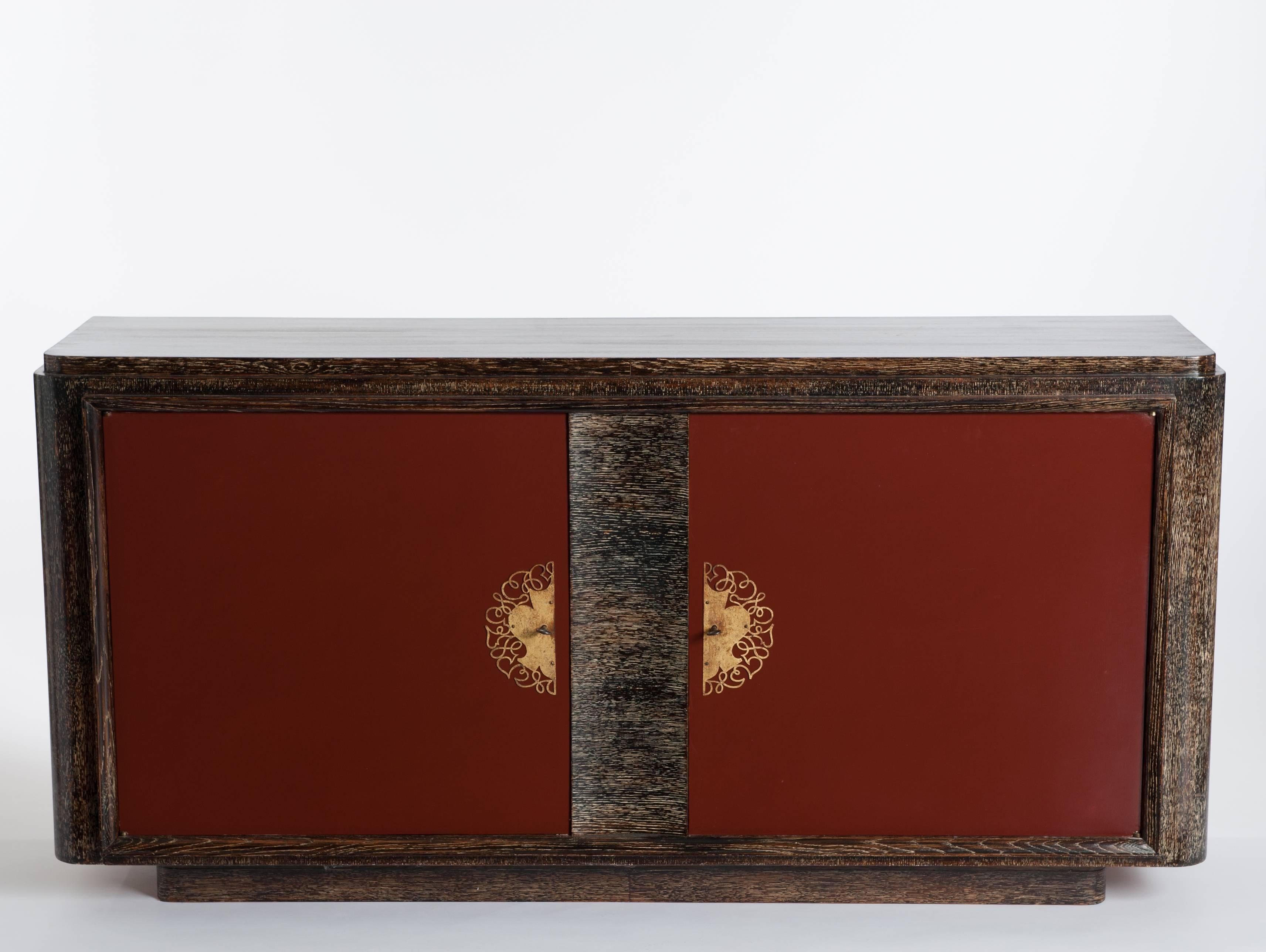 Two-door sideboard of the French Art Deco period in oak ceruse with 
dark red lacquered front part on a small socle (10cm). 
The gilded bronze garniture has a wonderful patina.