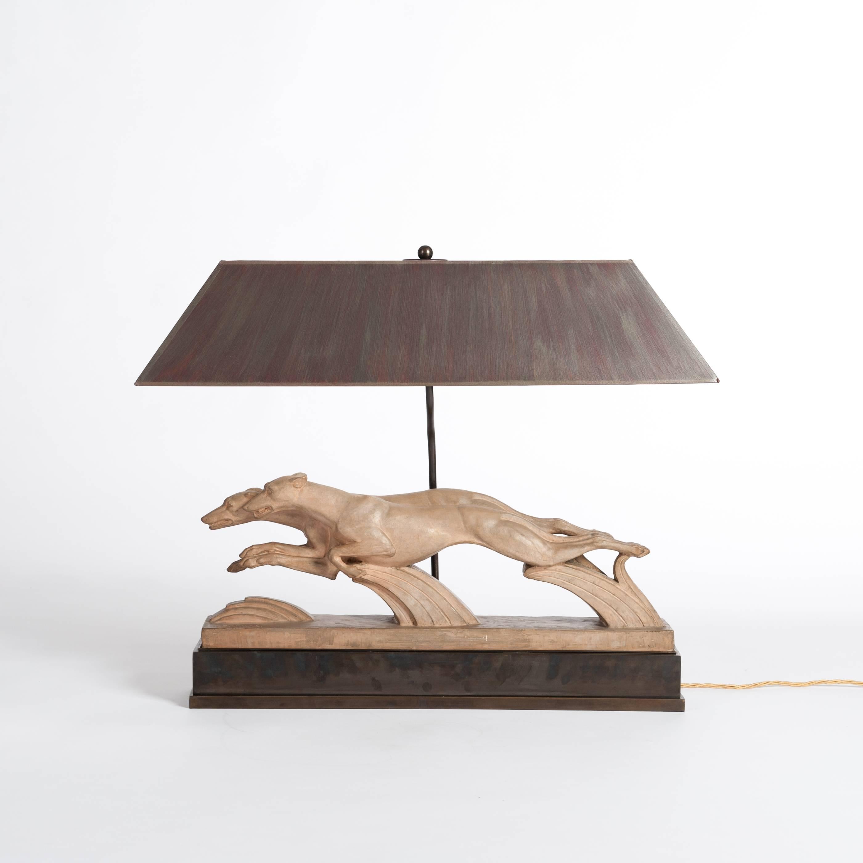 Very fine Art Deco cast terracotta sculpture from France with a purpose built lamp construction and socle in bronze.
Sujet: Patinated Art Deco greyhounds on the move, handsigned H. BARGAS
The rectangular lampshade is hand-painted in grey, red, brown