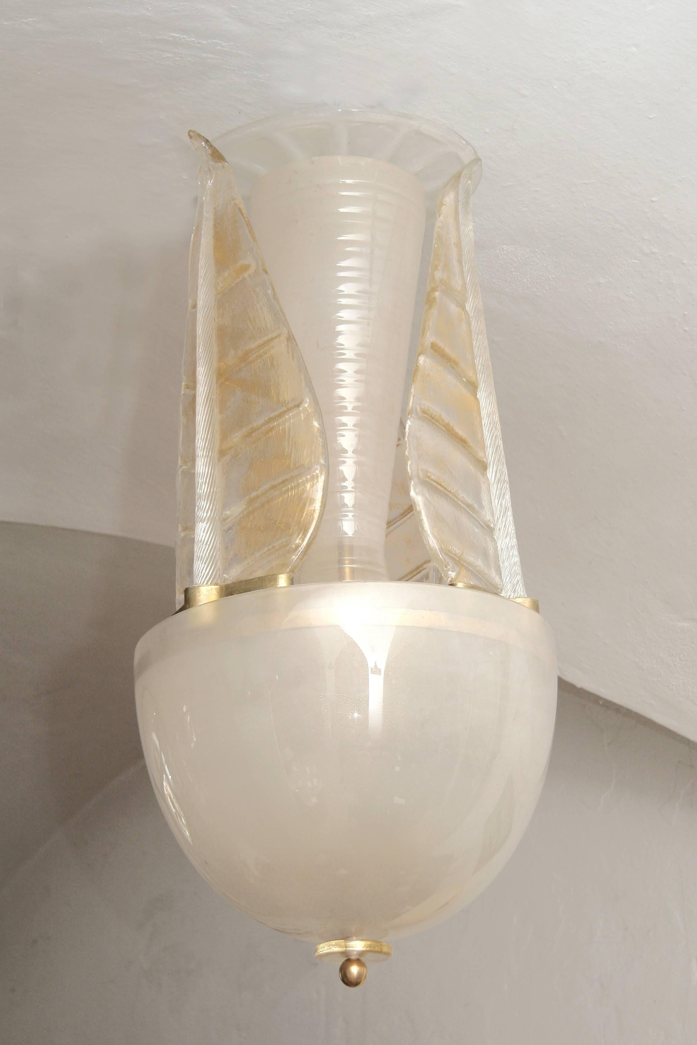 Elégant lustre en verre de Murano avec de fines particules d'or dans le lot de verre.
Trois grandes feuilles embrassant la tige centrale, un globe terrestre de 45 cm de diamètre
enlace l'électrification à trois lumières et complète la forme du