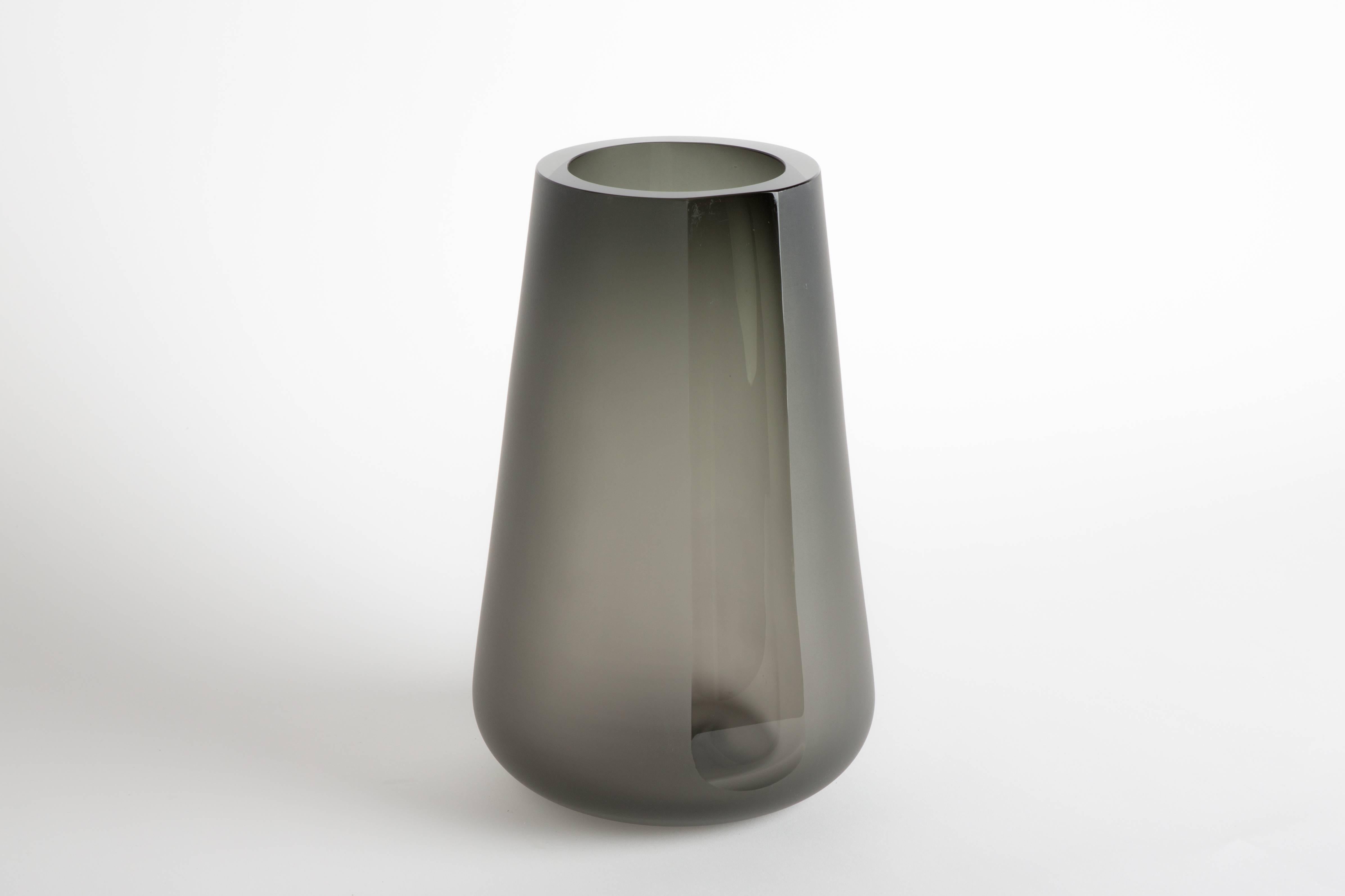 The Porto vase extra large is a simple exercise in optics and color. The Smoke Grey color and reflective light are diffused by a surface etching. A single panel, or "porto" is carved and brought to an optical polish on the side allowing