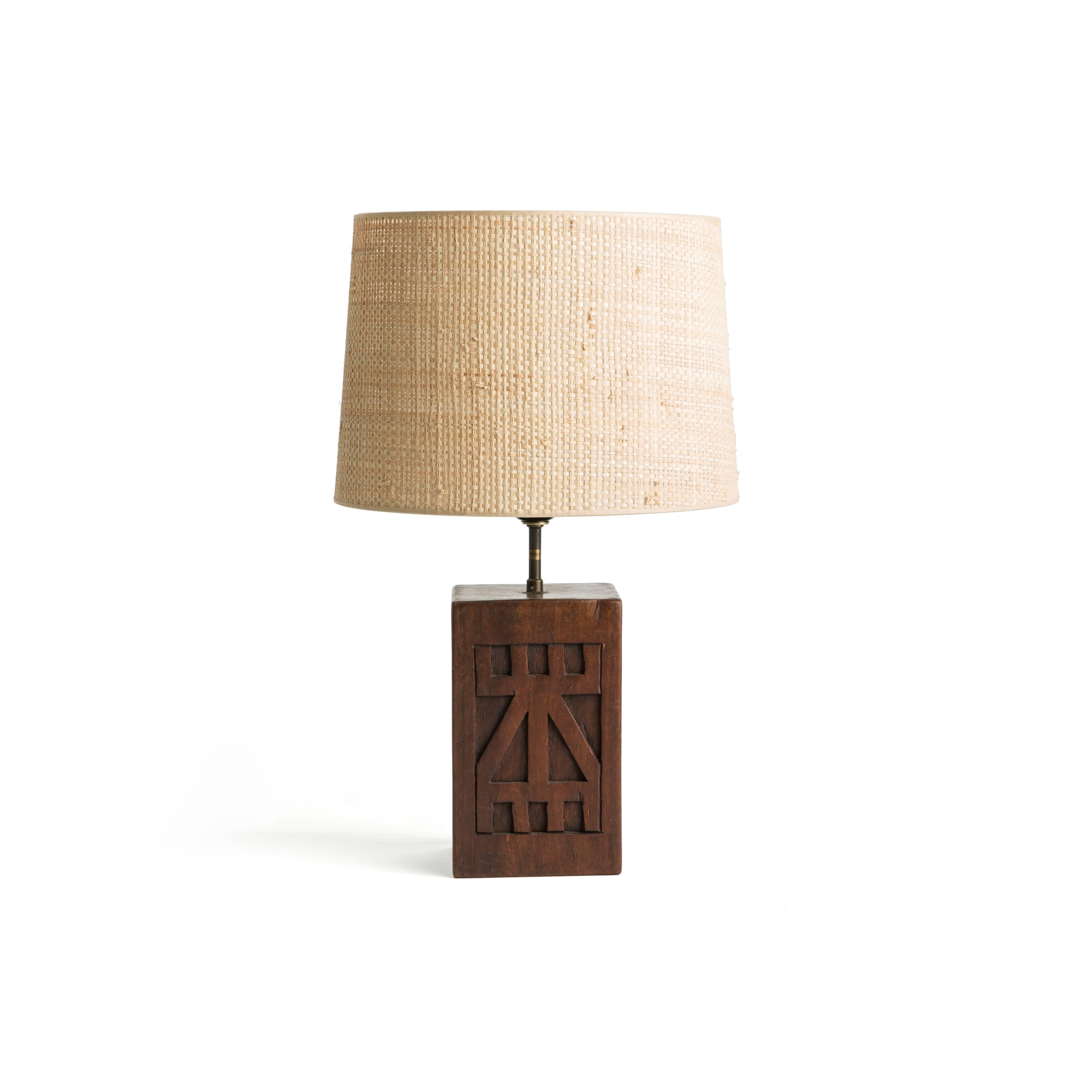 Hand-carved table lamp with a face on one side and a pattern on the opposite. 

Wired to US standards.

Woven shade included.