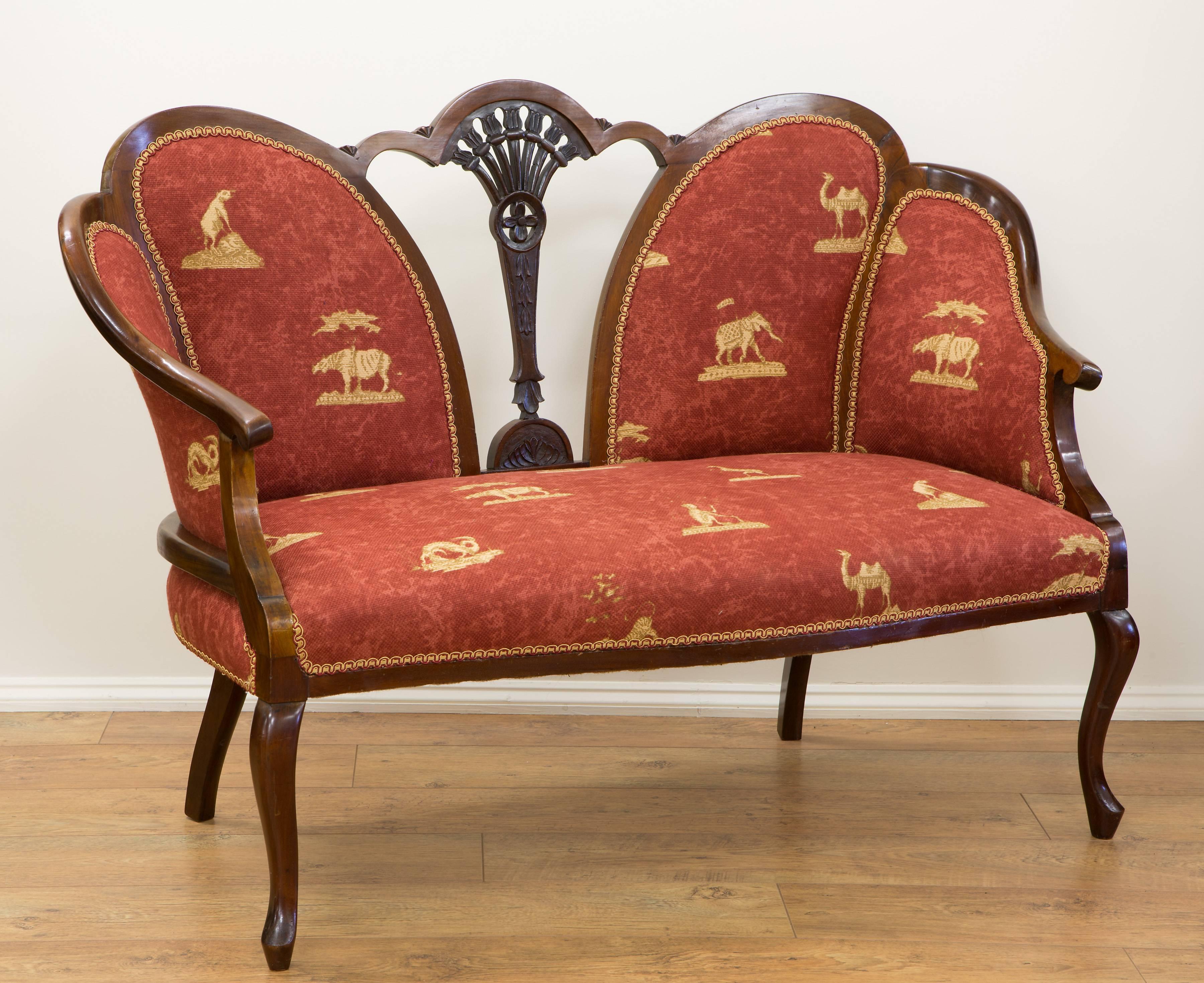 Edwardian mahogany two-seat settee with carved decoration and cabriole legs. Upholstered in red 'Livingstone' from the Atlas collection by Andrew Martin, circa 1900.