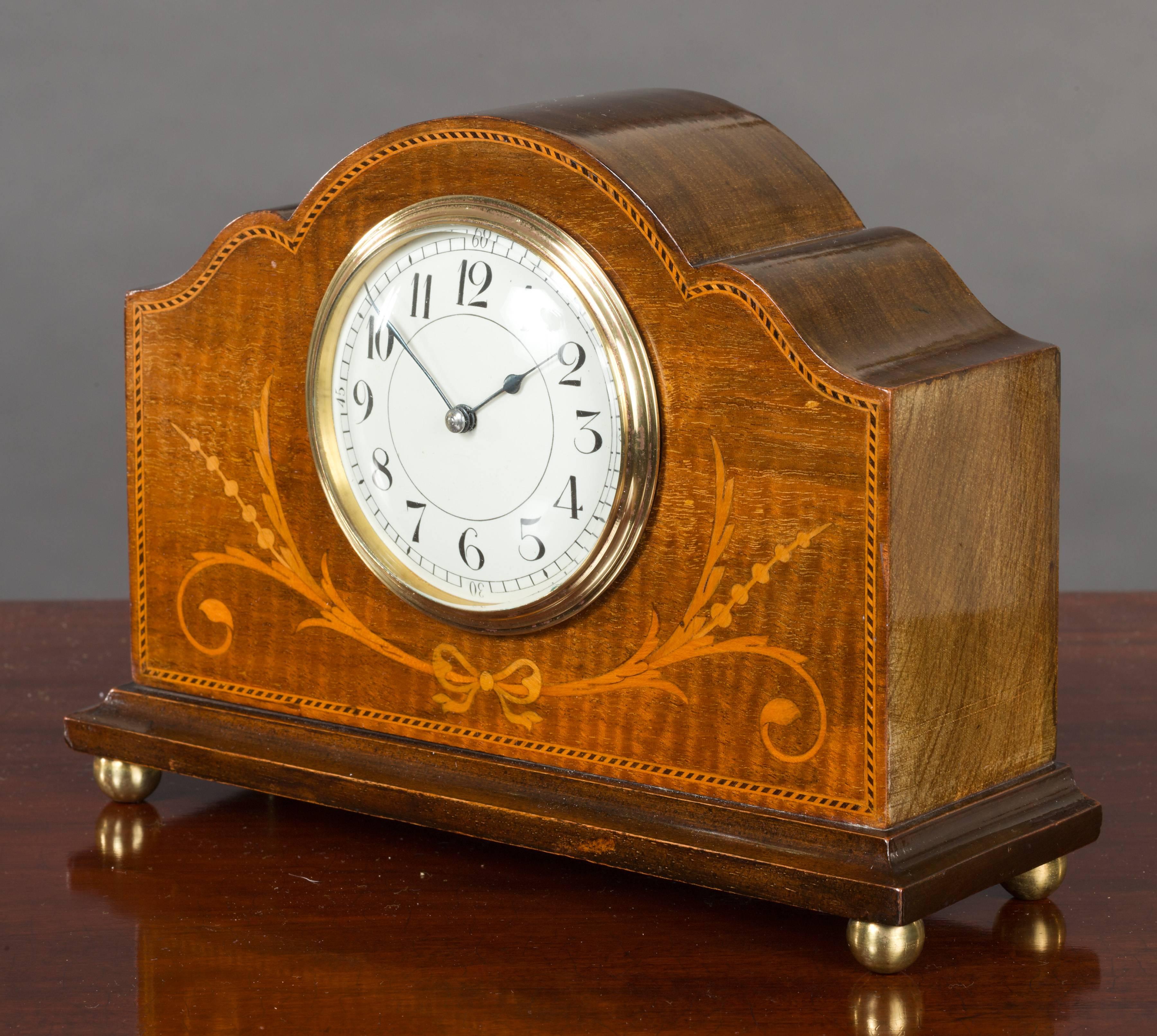 Edwardian mahogany mantel clock in a serpentine top case with boxwood and ebony chequered stringing and satinwood swag decoration resting on brass bun feet.

Enamel dial with Arabic numerals and original ‘blued’ steel hands.

Eight day French