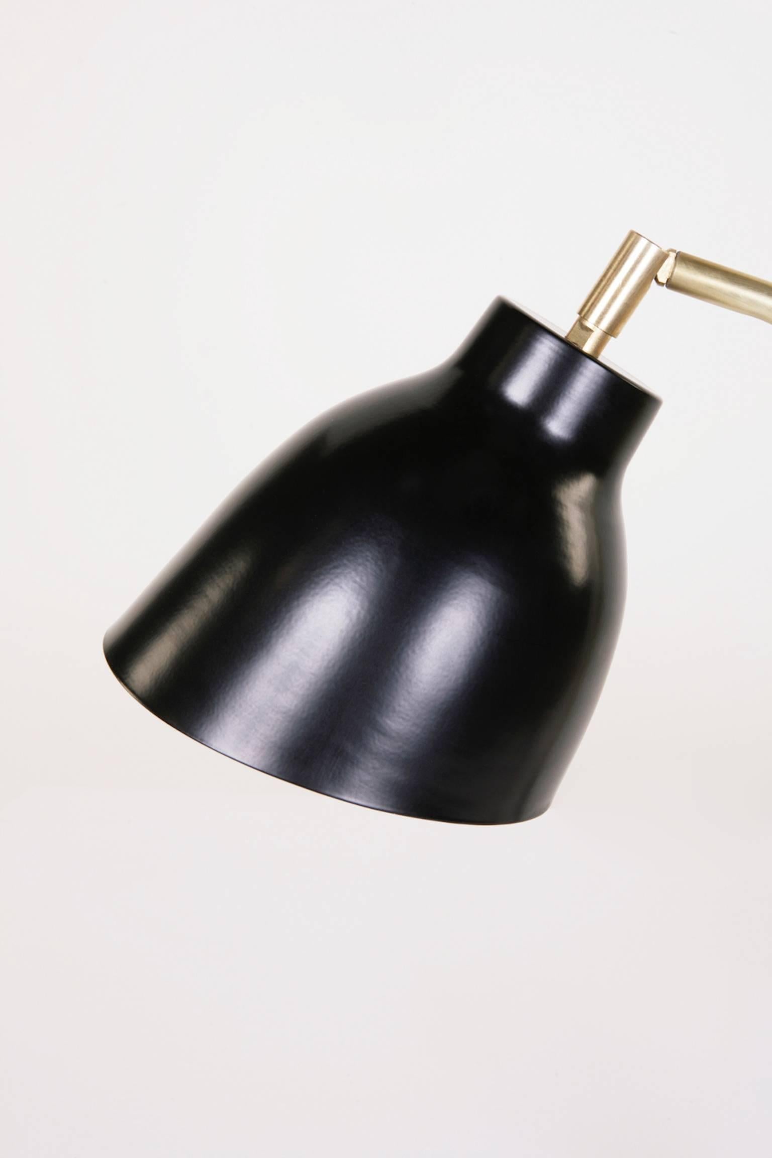 The Navire table lamp is part of Atelier de Troupe's classic Navire collection inspired by nautical lamps from the 1930s. The lamp has an adjustable solid brass arm and a tilting brass shade that is finished in a black powder coat. The lamp is wired